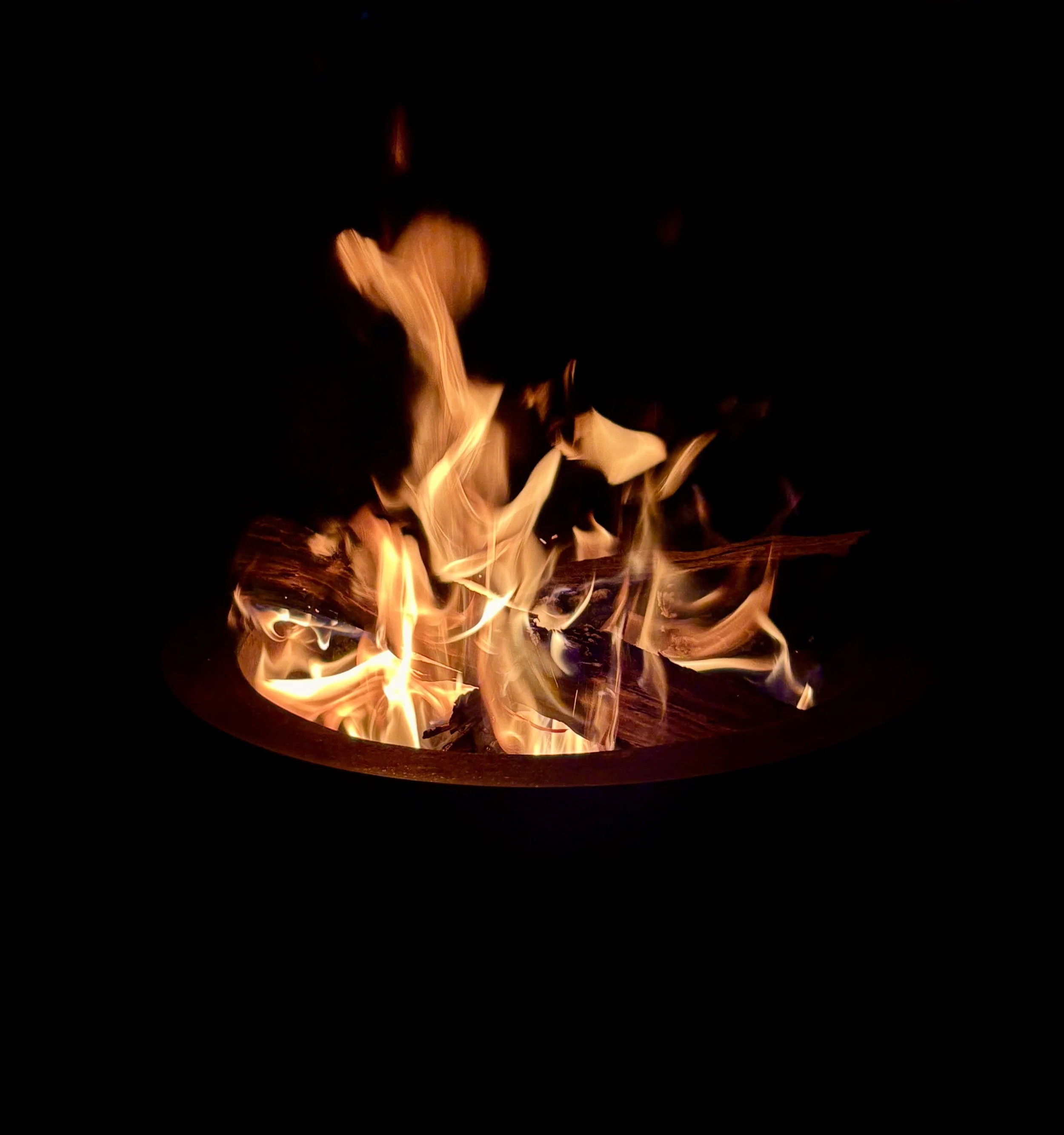 Firelight and flames rising from a dark fire pit at night