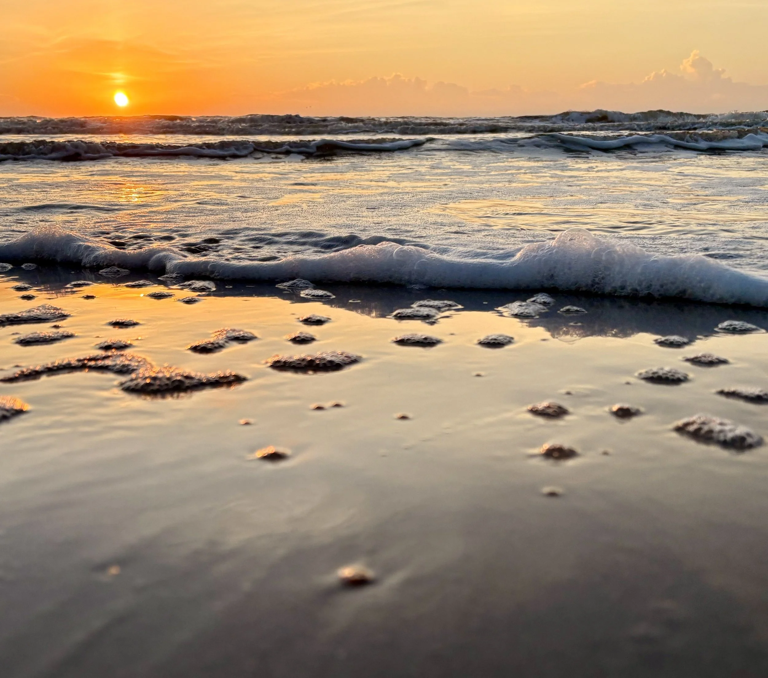 Sunset over the ocean reflected in tidal pools on a quiet beach