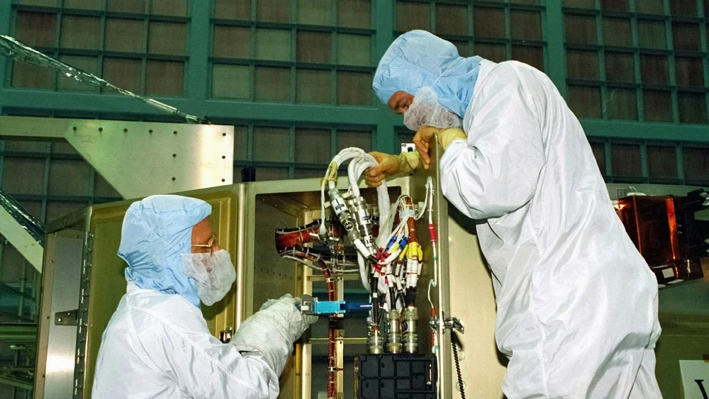 Technicians in clean room suits wiring spacecraft hardware