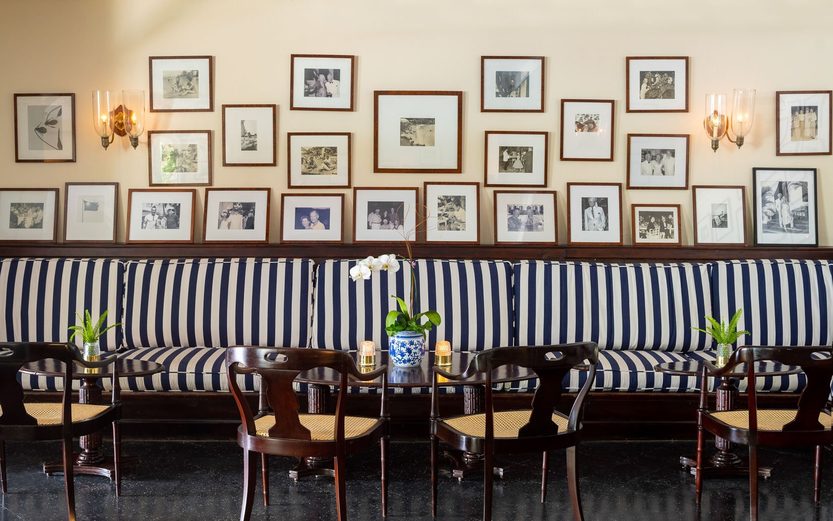 Round Hill interior featuring cane furniture, dark timber, and a gallery wall of historic photographs reflecting the Jamaican estate’s history.