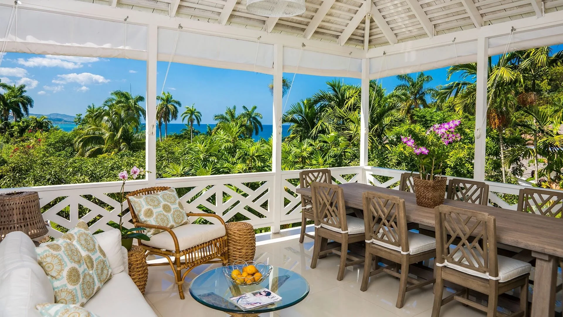 Open-air veranda at Round Hill in Jamaica, with louvered shutters, cane seating, columns, and tropical gardens beyond.
