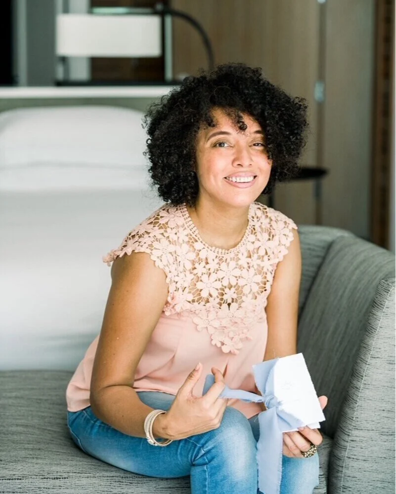 Tina Ebanks, designer behind Studio Two Sixteen, seated in her studio with wedding stationery in hand.