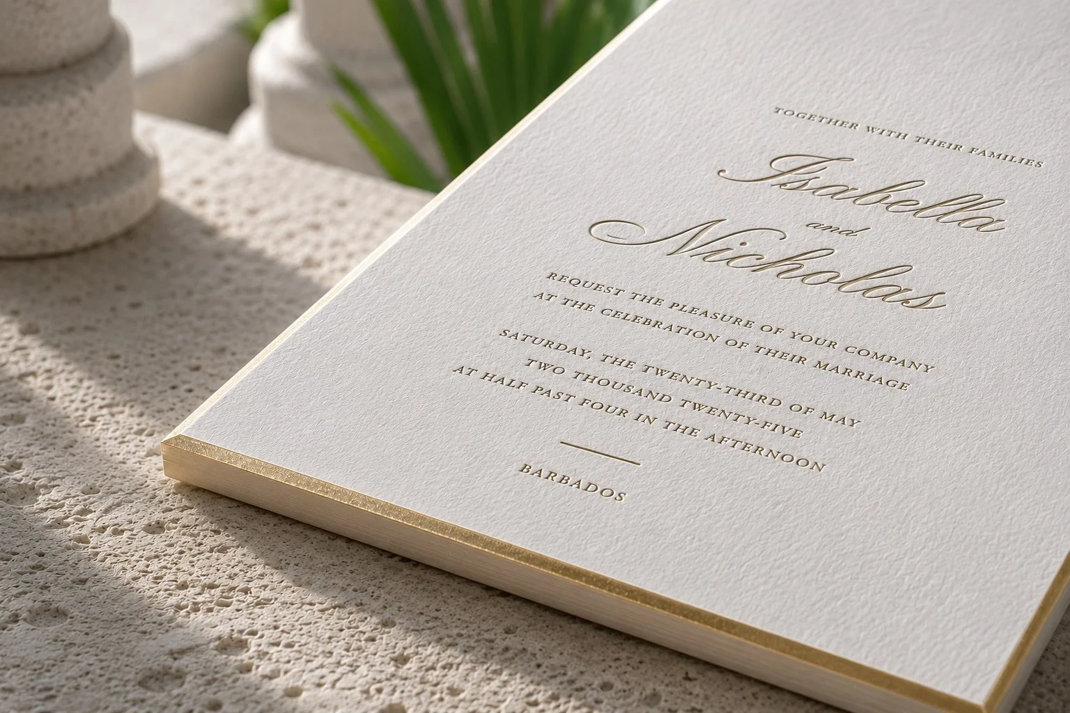 Close-up of a letterpress wedding invitation on textured paper with a fine gold gilded edge.