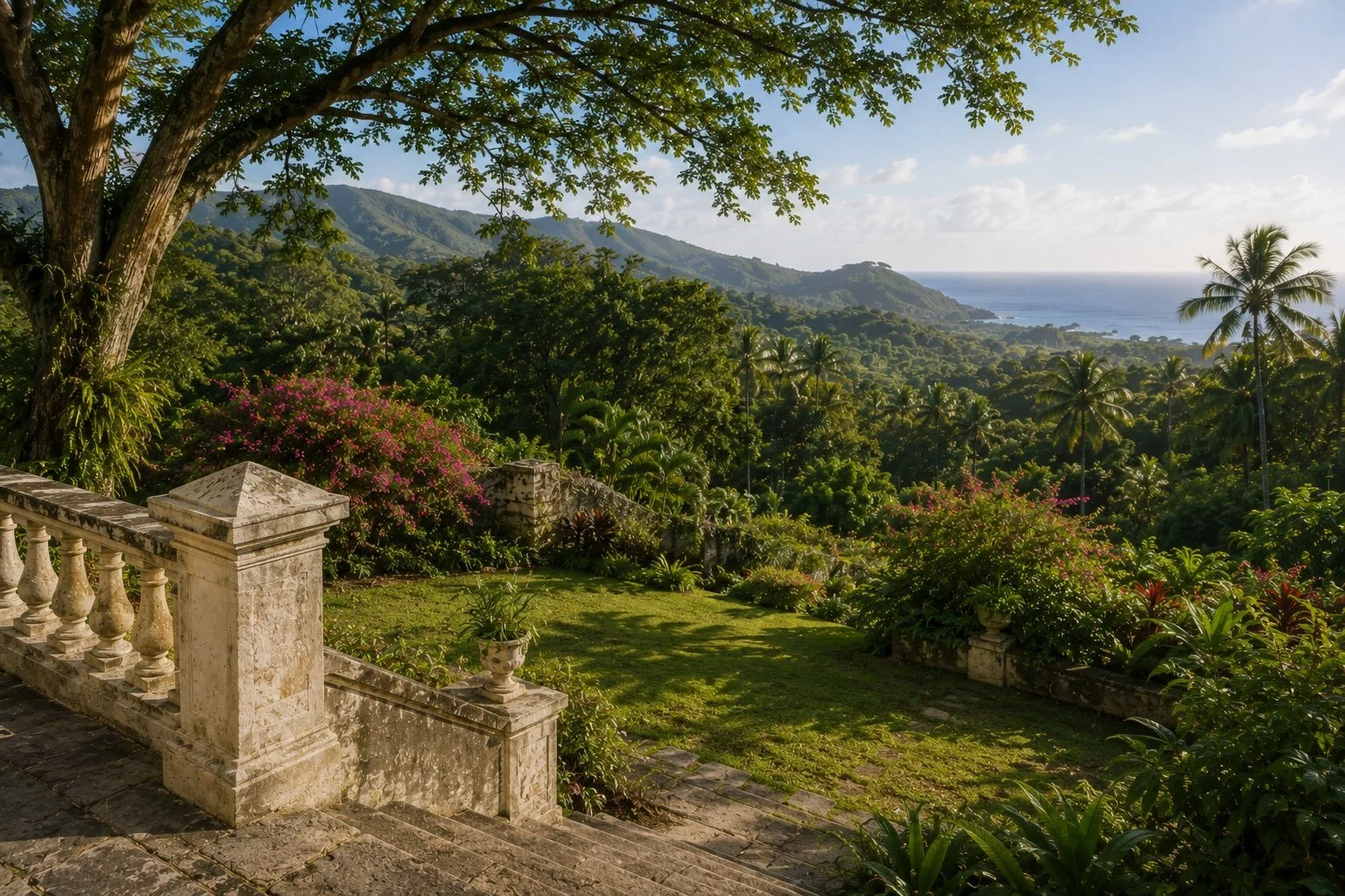 Tropical garden at a historic Jamaican estate, with stone steps, mature trees, flowering plants, and views toward the mountains and sea.