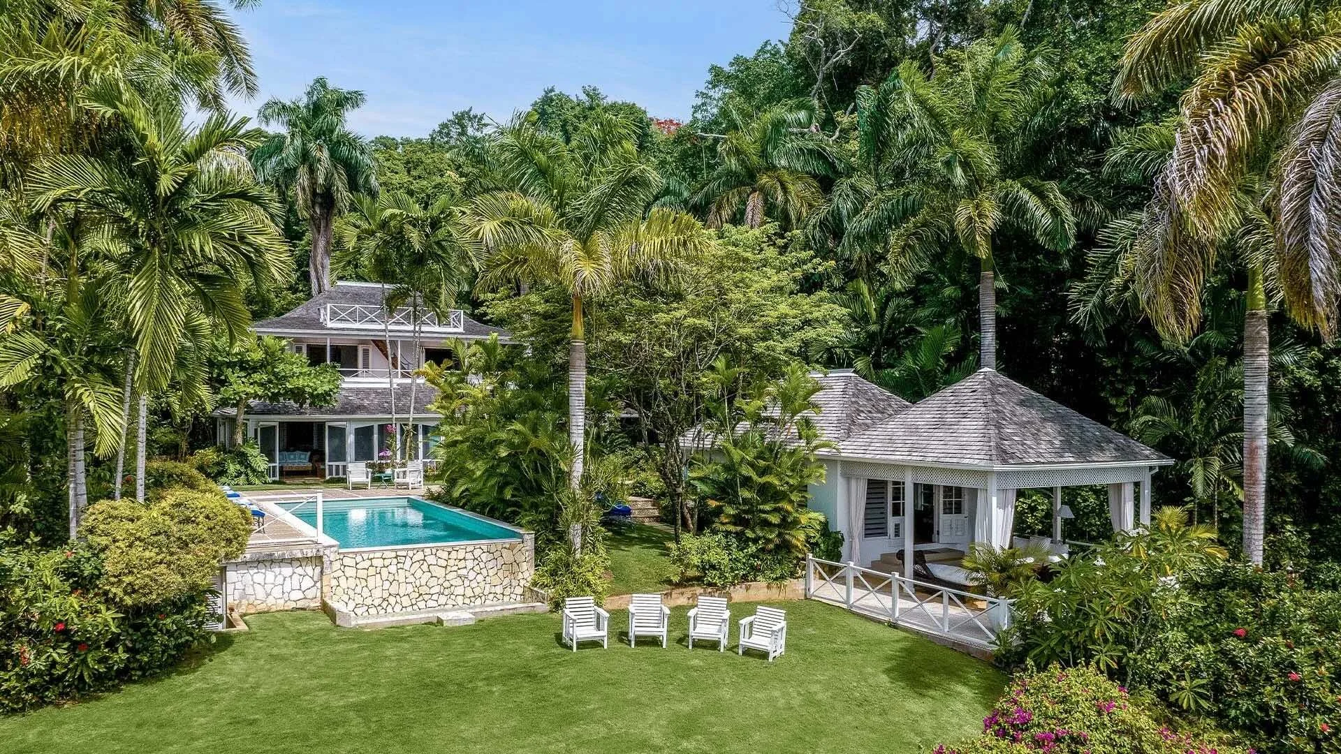 Round Hill villa in Jamaica with white timber architecture, pitched roofs, an open-air pavilion, pool, lawn, and tropical gardens.