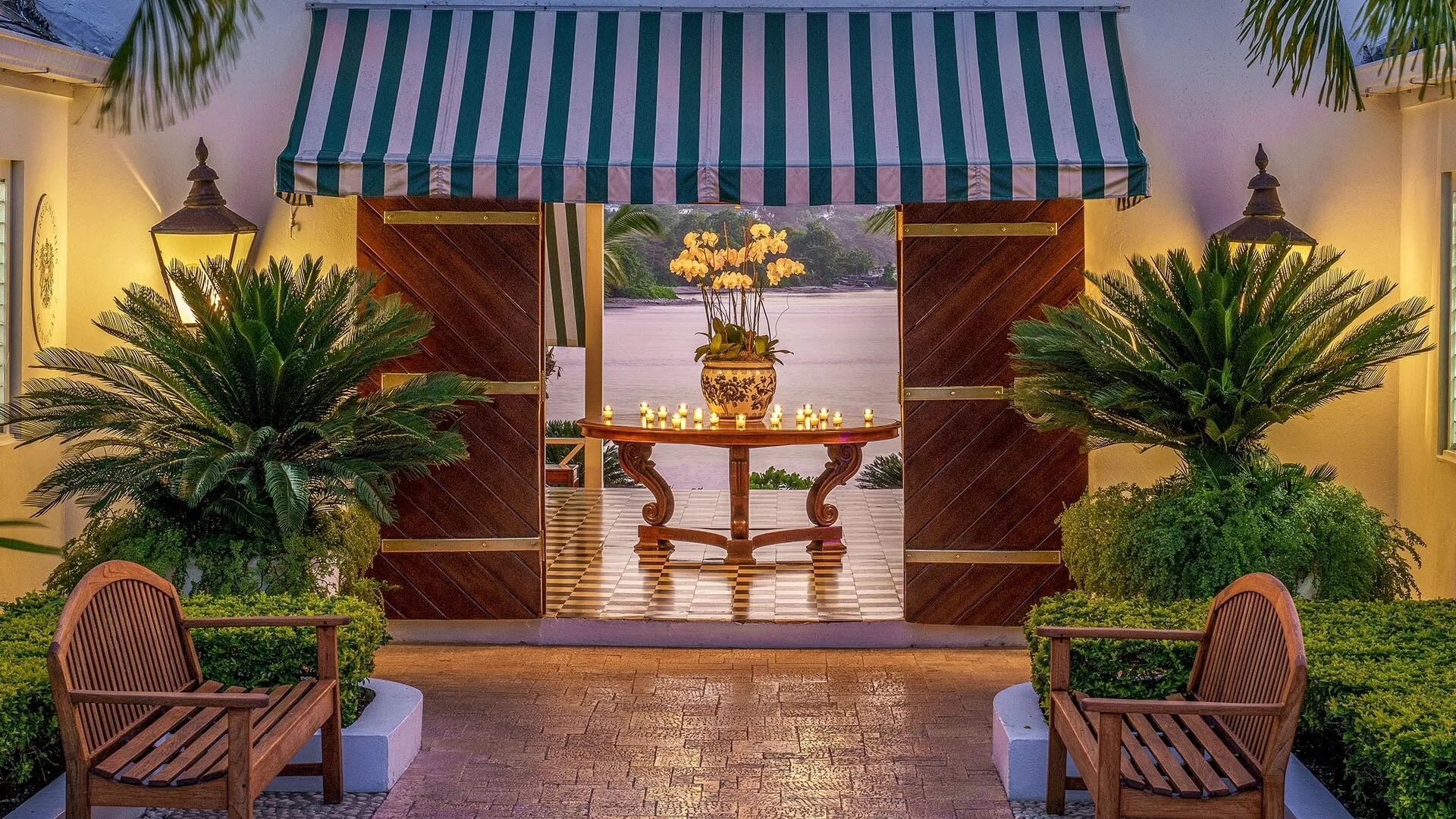 Architectural details at Round Hill in Jamaica, featuring dark timber gates, pale walls, tropical greenery, lanterns, and a patterned floor.