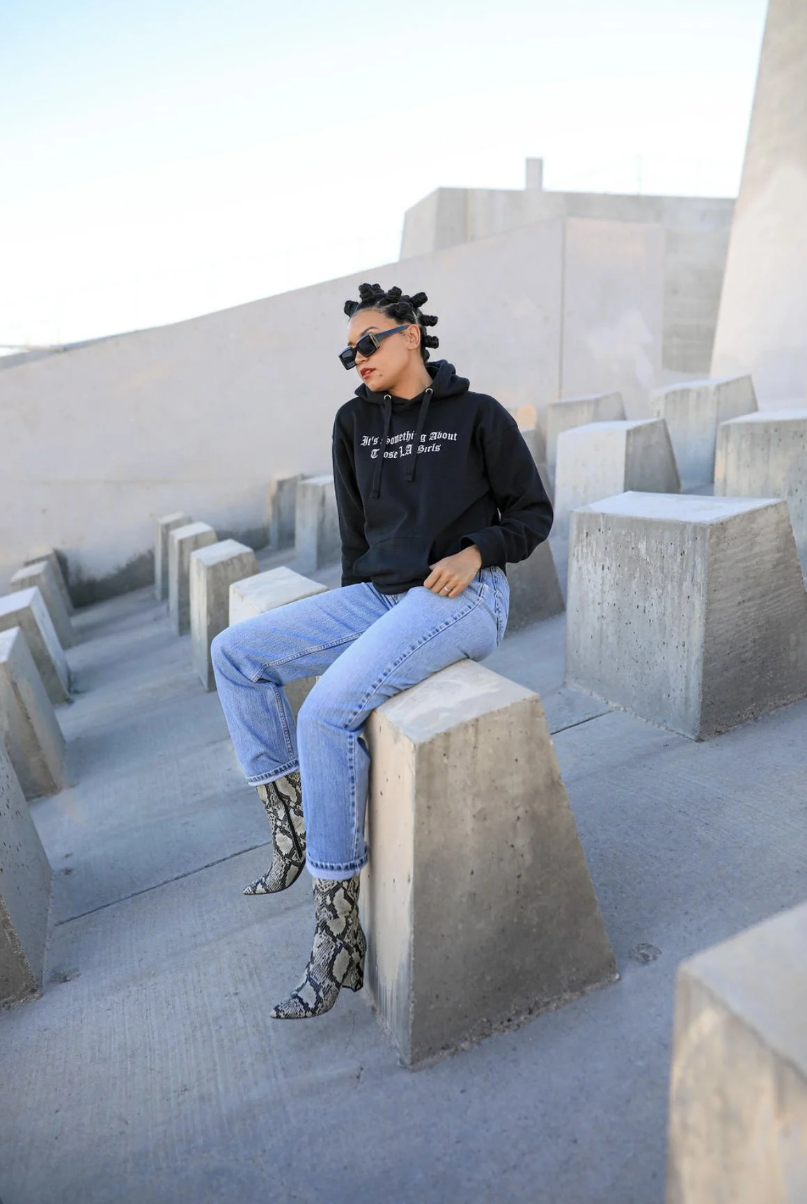 Person in sunglasses and casual outfit sitting on concrete blocks.