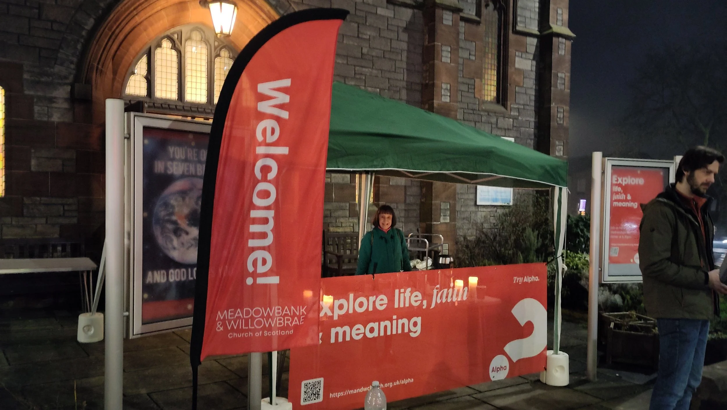 A gazebo set up outside the church building with a bright red banner attached to the front saying "Explore life, faith & meaning. Try Alpha."
