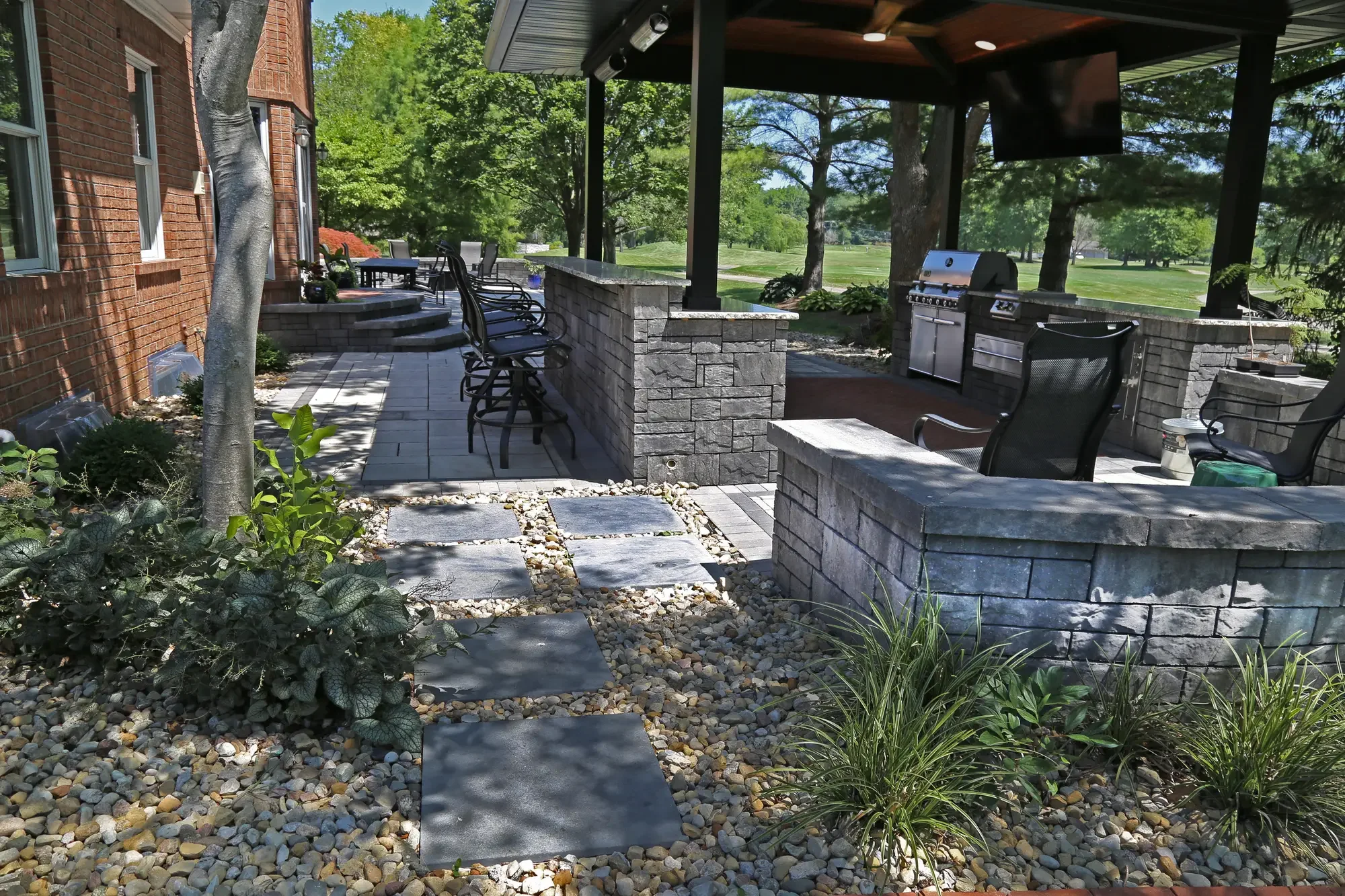 Stepping stone path through river rock bed leading to pavilion and outdoor kitchen with bar seating at The Wooded Pavilion by Green View in Illinois