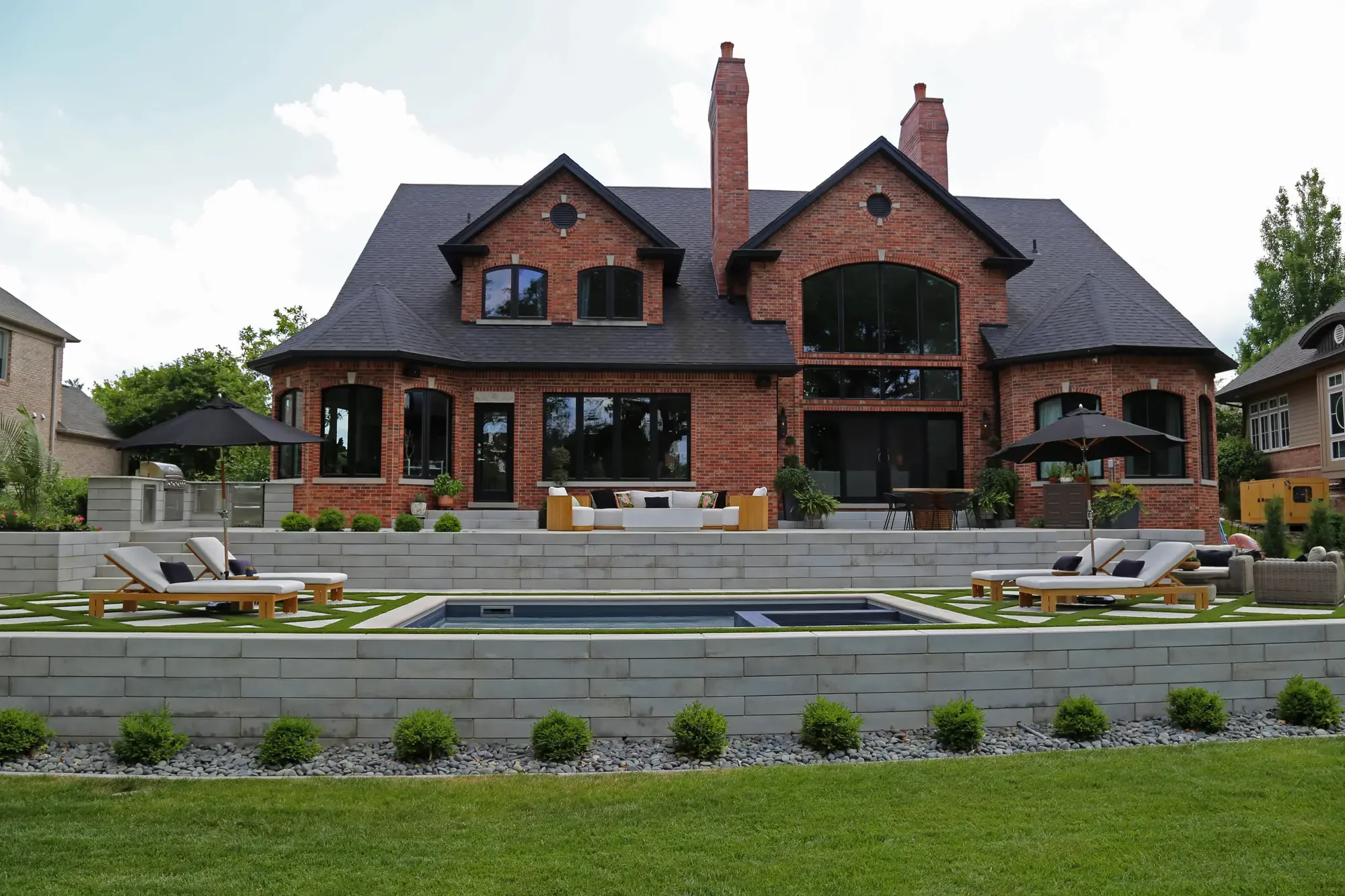 Full rear elevation of estate with pool, geometric turf-and-paver surround, tiered stone retaining walls, and chaise lounges at Geometric Oasis Retreat by Green View in Illinois