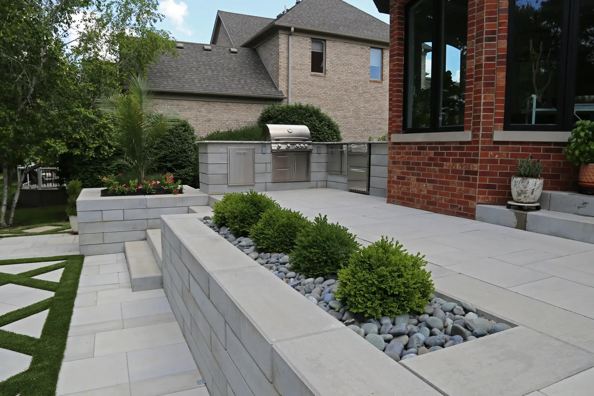 Raised stone planter with clipped boxwood and river rock adjacent to upper patio outdoor kitchen at Geometric Oasis Retreat by Green View in Illinois