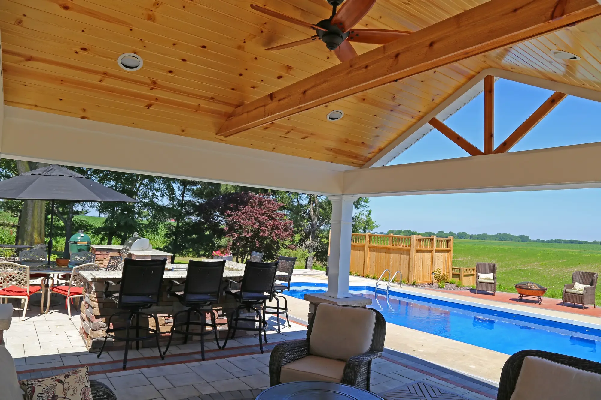 Interior view of metal roof pavilion with cedar ceiling, ceiling fan, granite bar seating, and pool with open farmfield view at The Prairie Pavilion by Green View in Illinois