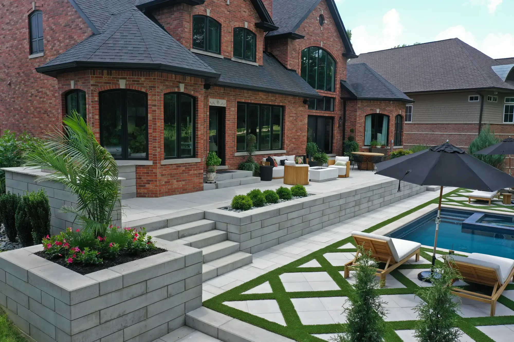 Upper patio with lounge seating, fire table, and geometric turf-and-paver pool surround below at Geometric Oasis Retreat by Green View in Illinois