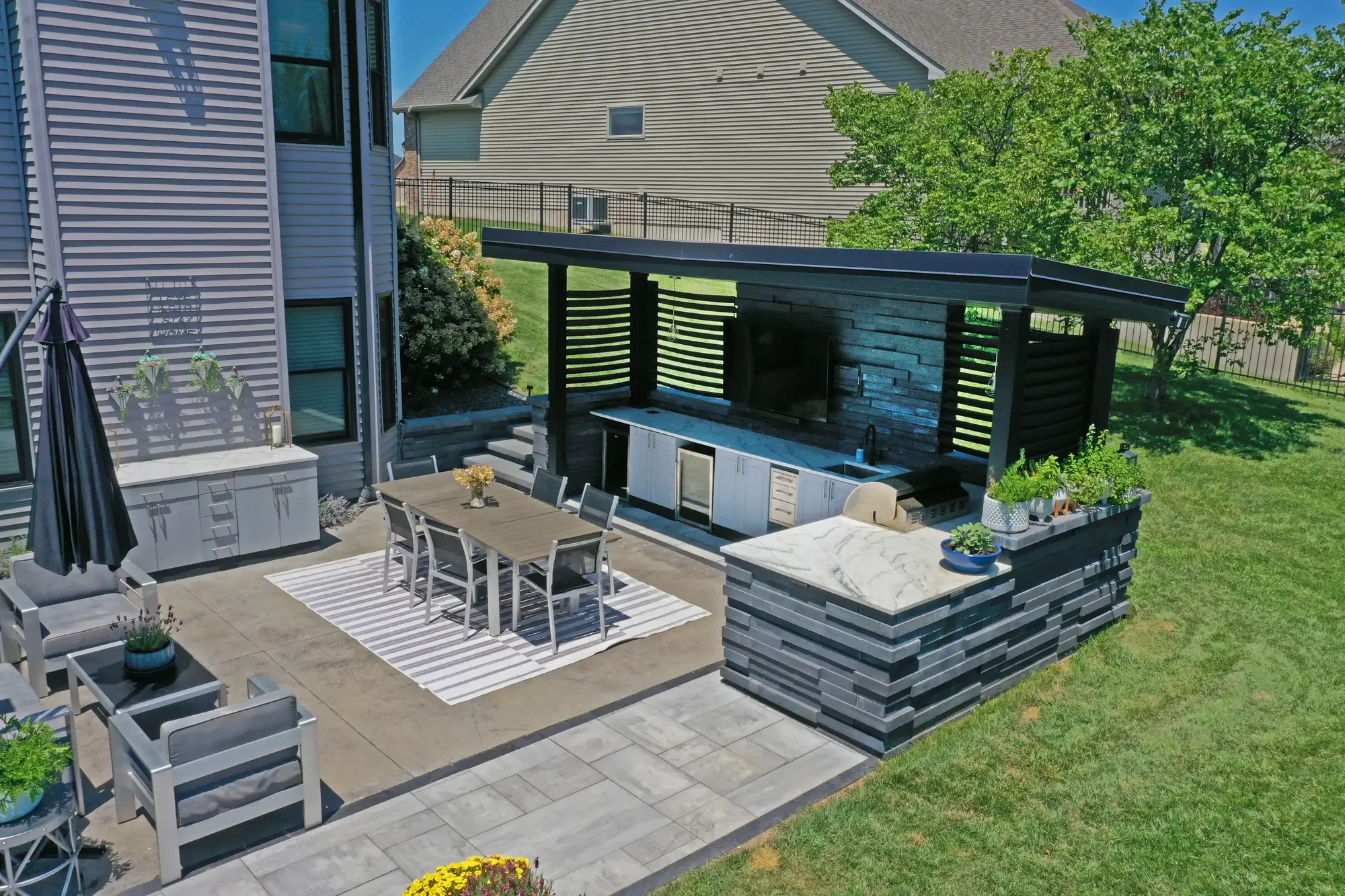 Overhead view of modern dark pergola with outdoor kitchen, marble bar top, and dining area at Slate and Steel by Green View in Illinois