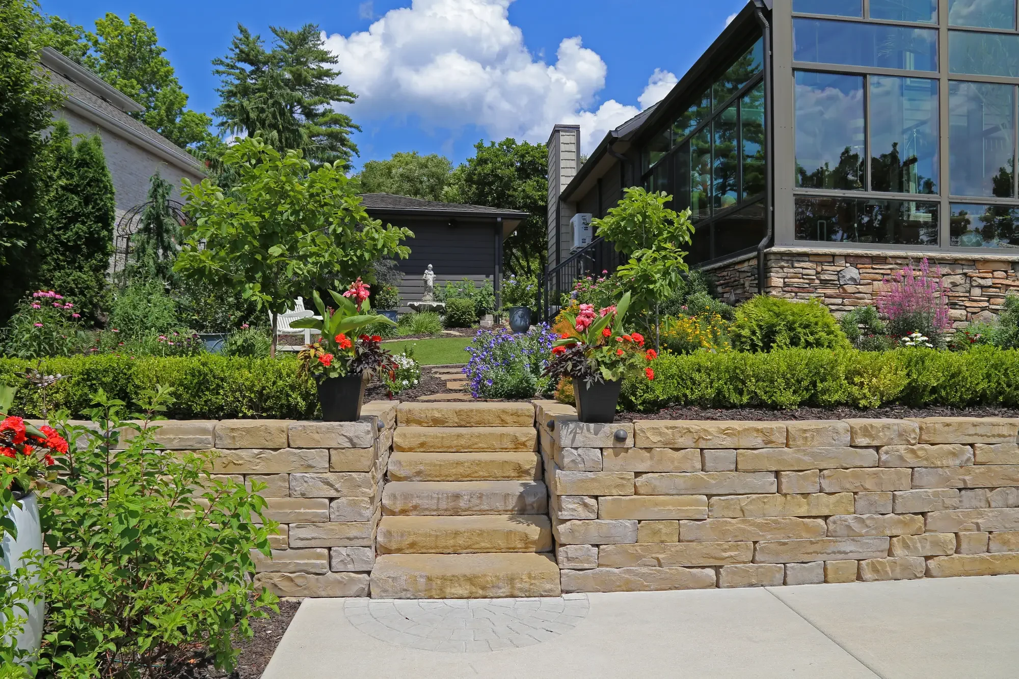 Natural stone retaining wall with steps, colorful container plantings, and greenhouse addition beyond at The Lakeside Garden by Green View in Illinois