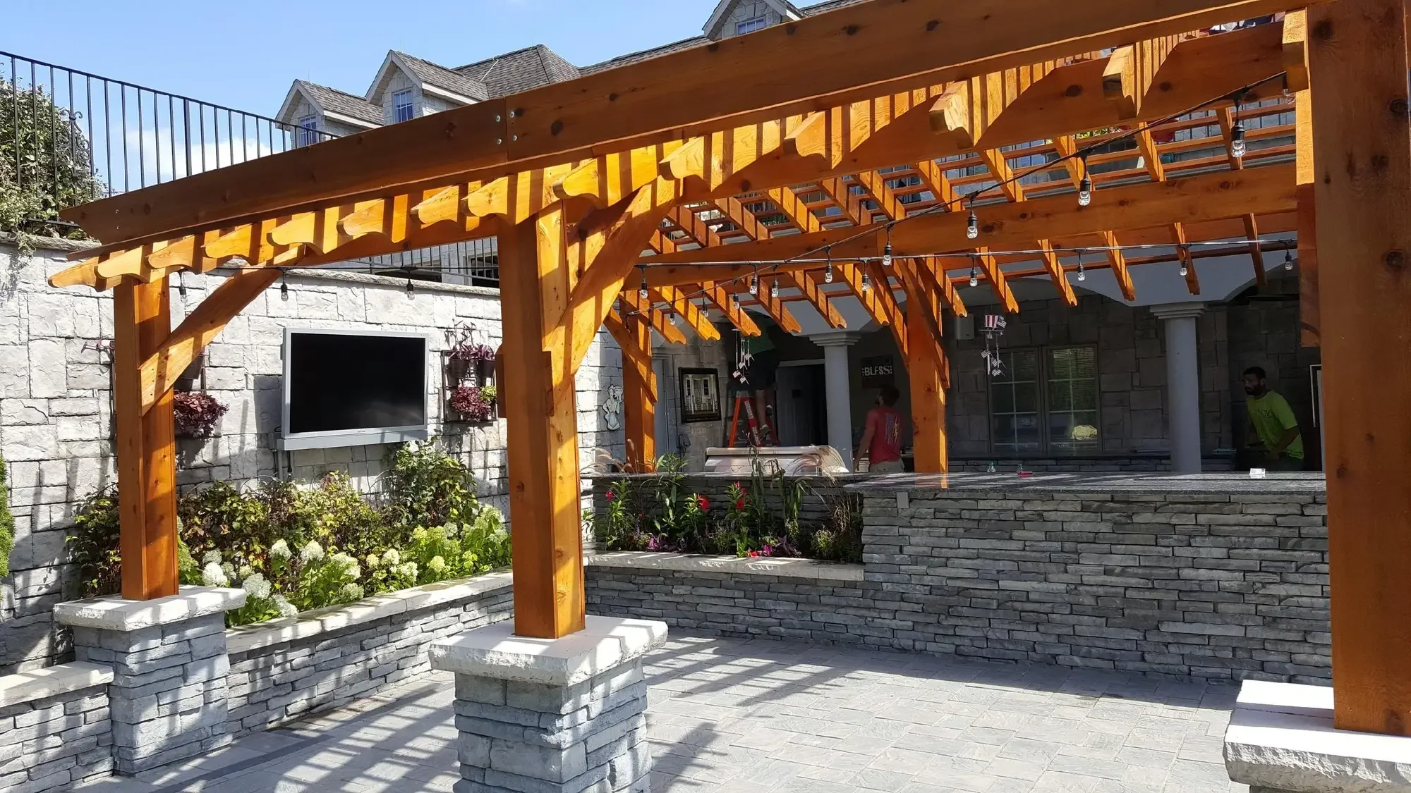 Cedar pergola structure with outdoor TV wall, stone columns, and lush perennial planting beds at The Craftsman's Retreat by Green View in Illinois