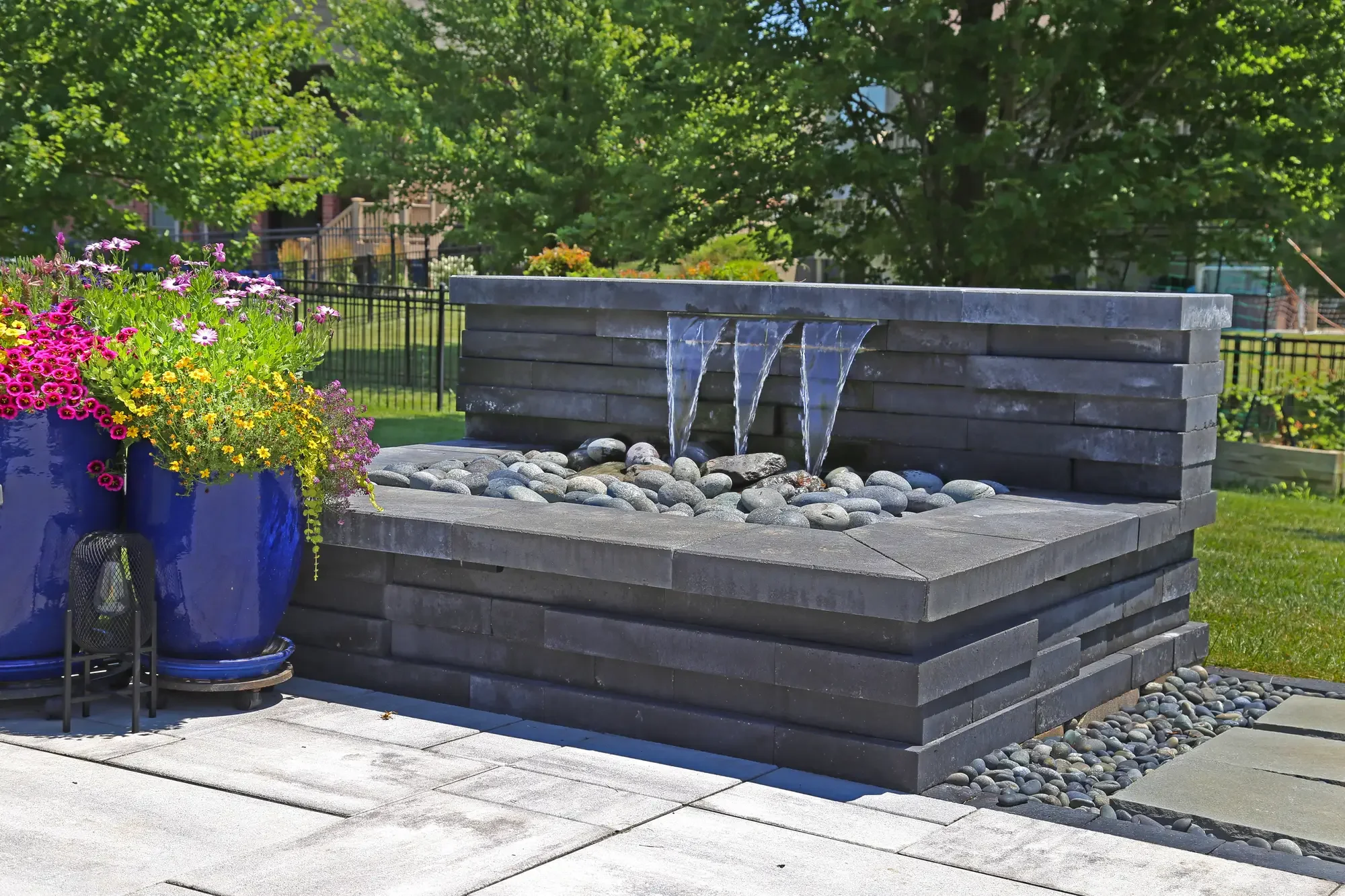 Modern dark stacked stone water feature with cascading spouts and river rock basin at Slate and Steel by Green View in Illinois
