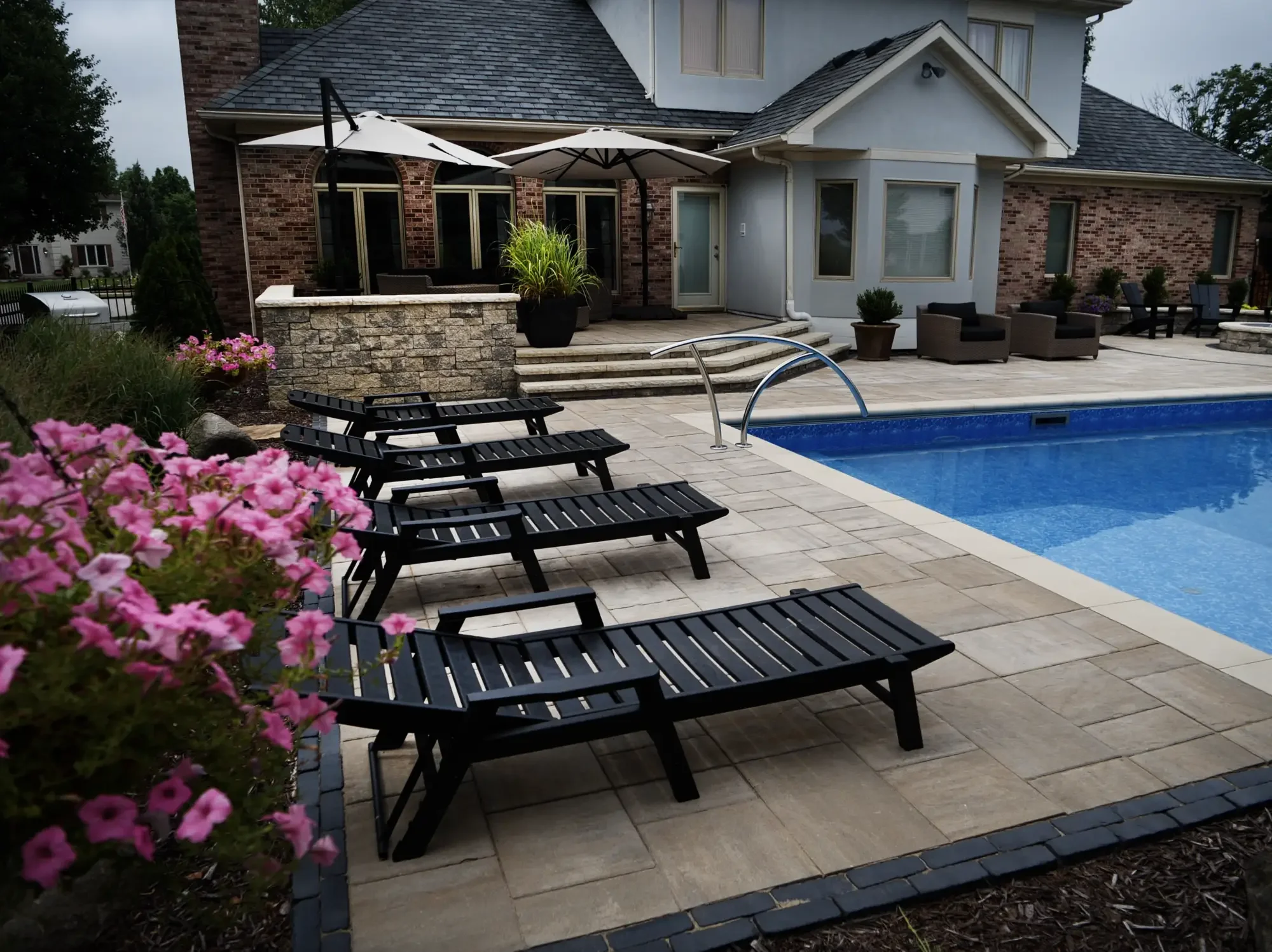 Paver pool surround with lush perennial planting beds, stone walls, and fire pit by Green View in Illinois