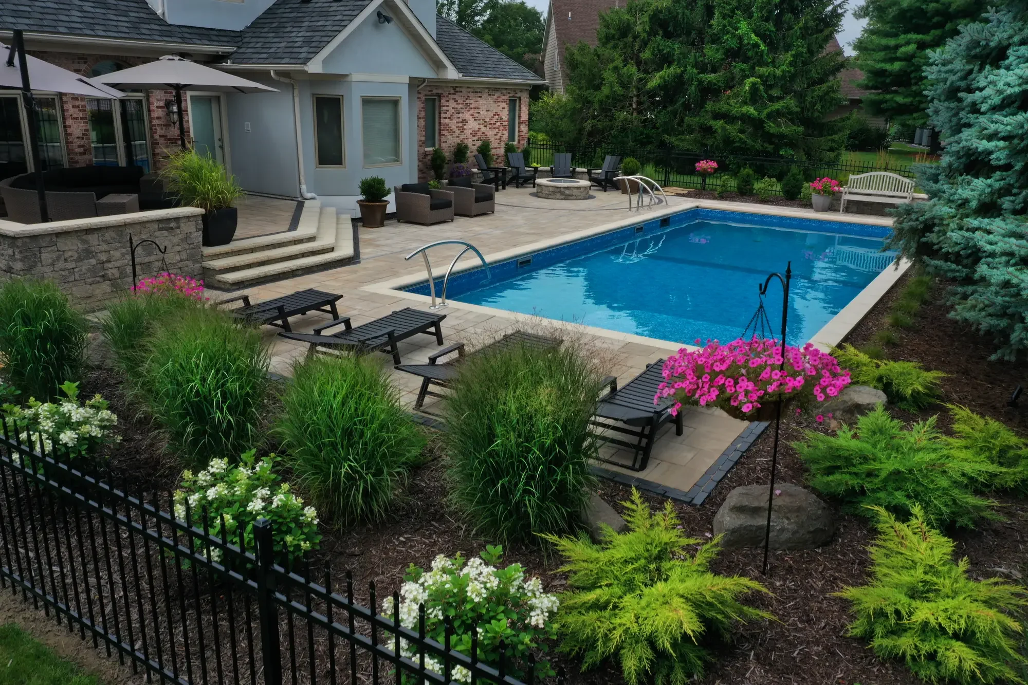 Stone garden wall with ornamental grasses and perennial planting along pool surround by Green View in Illinois