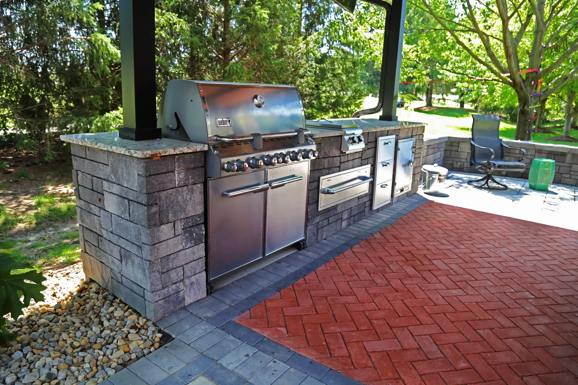 Outdoor kitchen with built-in grill, stainless appliances, and granite countertop under pavilion at The Wooded Pavilion by Green View in Illinois