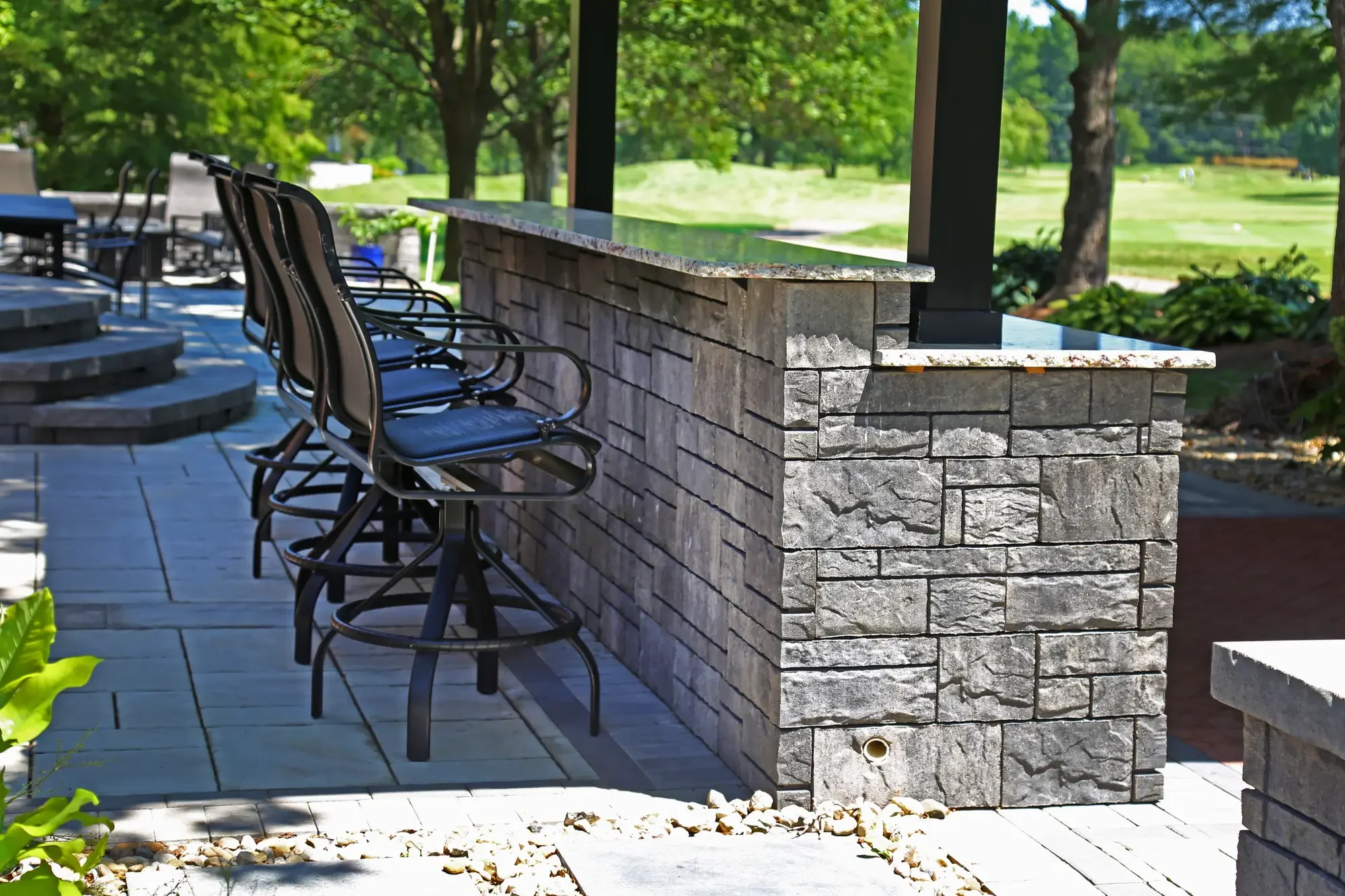 Stone bar wall with granite countertop and row of bar stools overlooking golf course at The Wooded Pavilion by Green View in Illinois