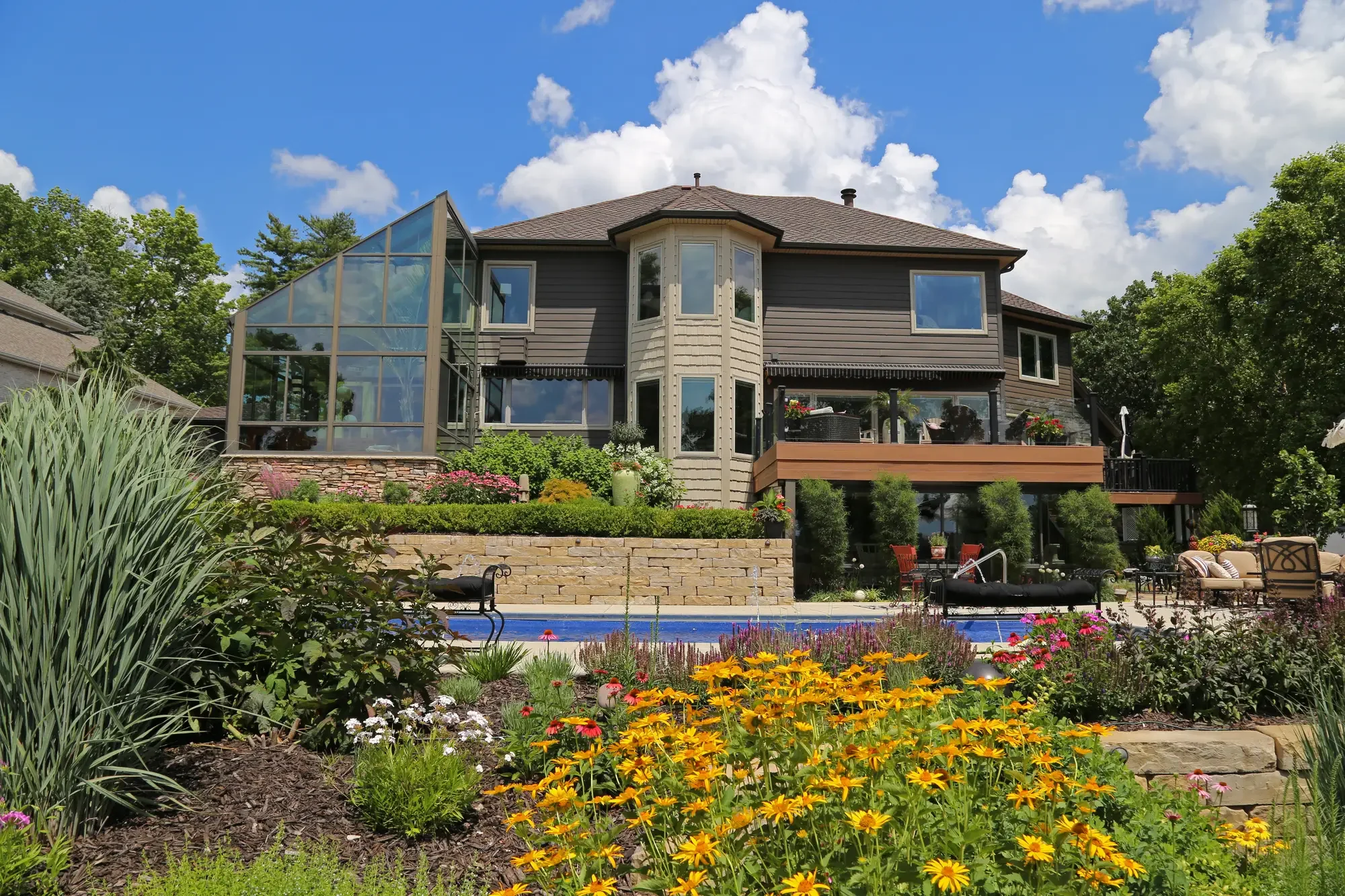 Estate rear elevation with greenhouse addition, tiered natural stone retaining wall, and perennial planting beds at The Lakeside Garden by Green View in Illinois