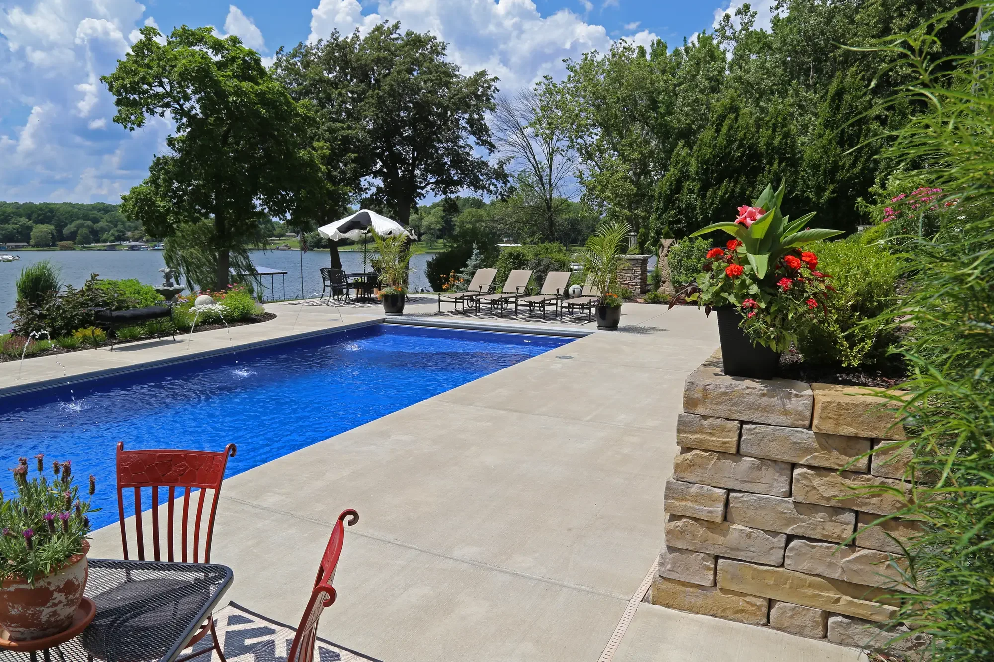 Pool with concrete surround, natural stone retaining wall, tropical container plantings, and open lake view at The Lakeside Garden by Green View in Illinois