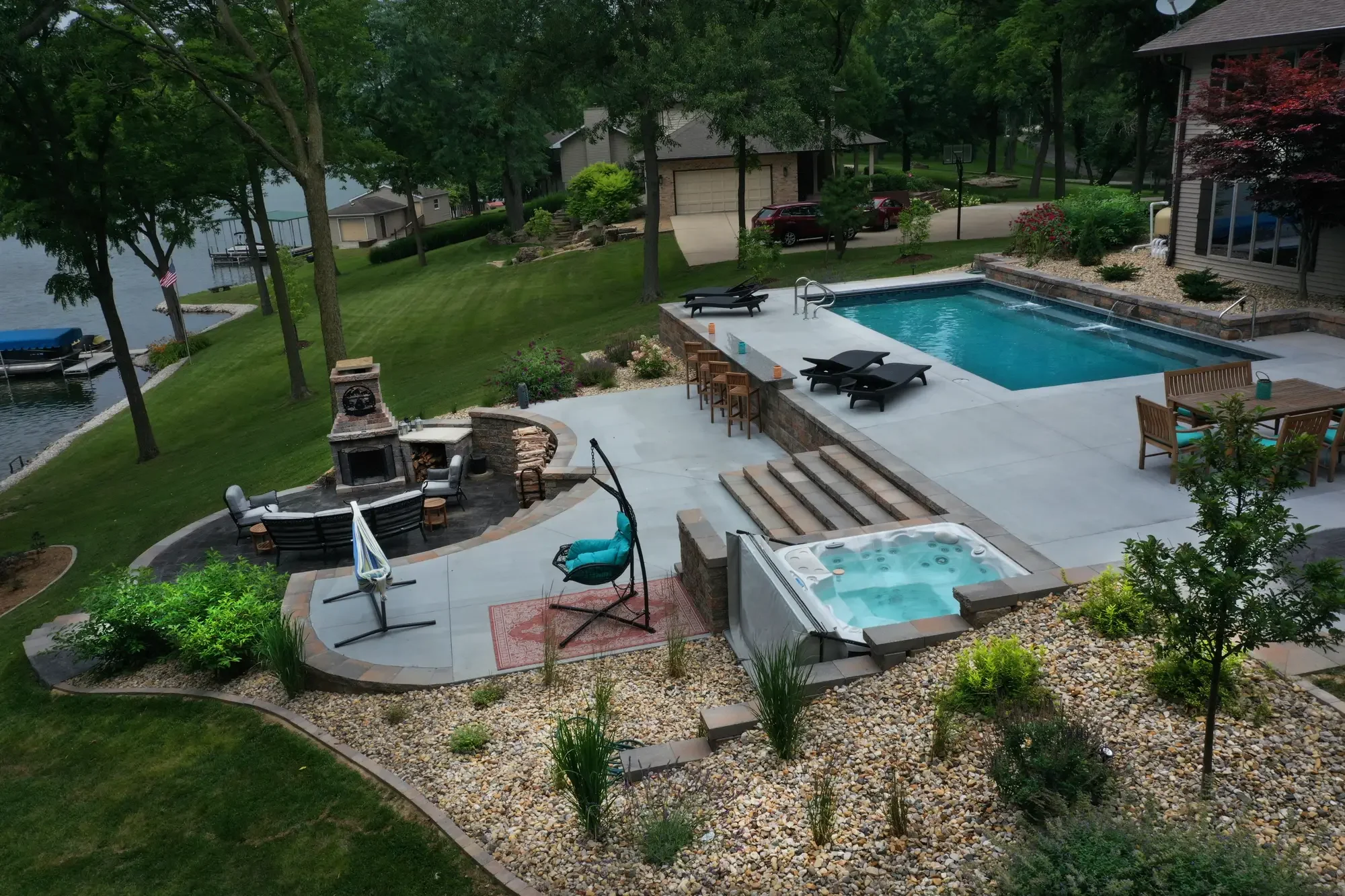 Lakefront aerial view of pool surround, outdoor fireplace, inset hot tub, and planting beds at The Amphitheater by Green View in Illinois