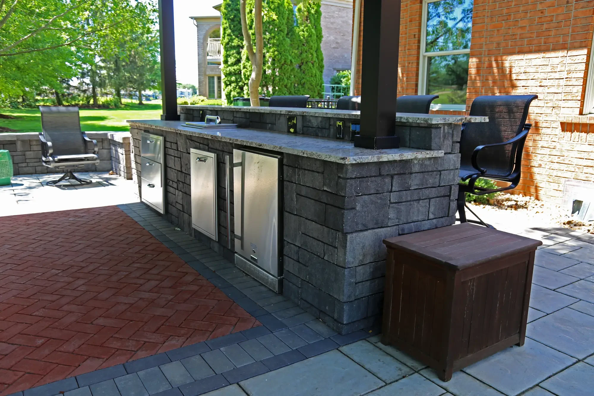 Stone outdoor bar with built-in refrigerator, granite countertop, and bar seating at The Wooded Pavilion by Green View in Illinois