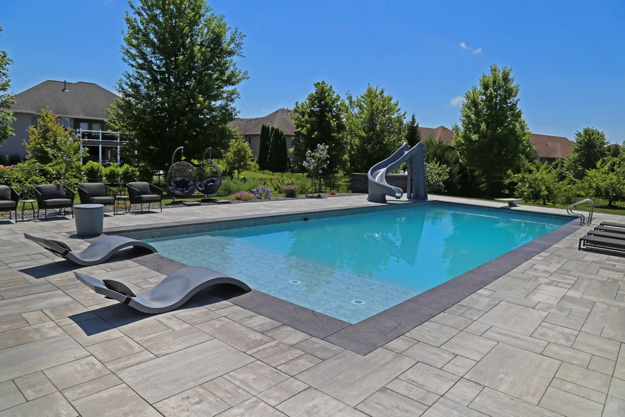 Rectangular pool with water slide, modern chaise lounges, and large-format paver surround at Slate and Steel by Green View in Illinois
