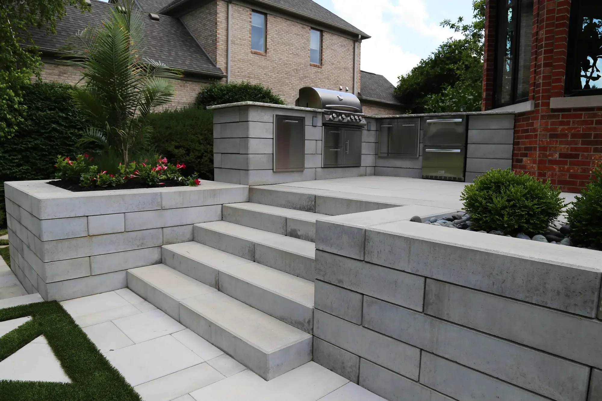 Tiered stone retaining wall steps leading to upper patio with built-in outdoor kitchen at Geometric Oasis Retreat by Green View in Illinois