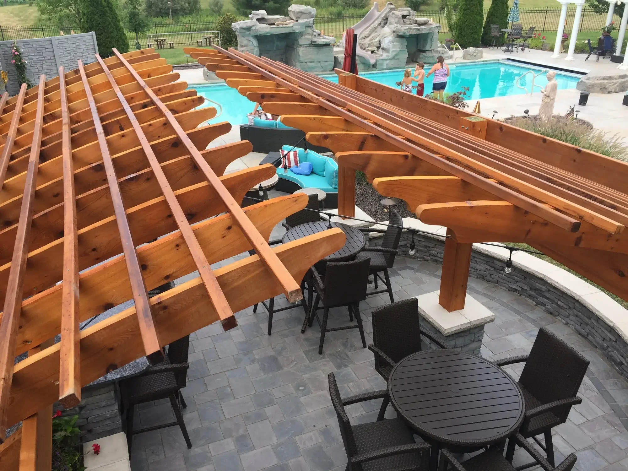 Overhead view of arched cedar pergola roof structure with paver patio, seating areas, and pool beyond at The Craftsman's Retreat by Green View in Illinois
