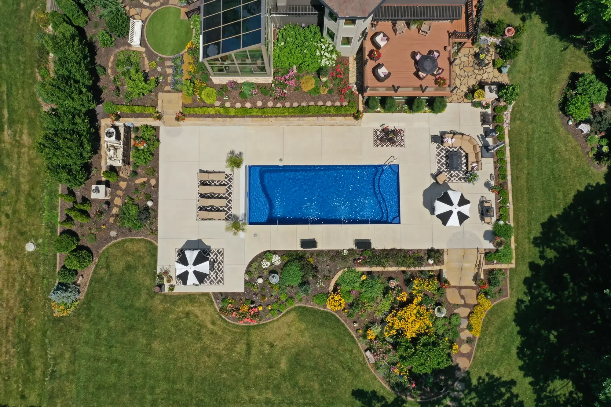 Aerial view of lakefront estate with rectangular pool, greenhouse addition, wood deck, perennial garden beds, and flagstone paths at The Lakeside Garden by Green View in Illinois