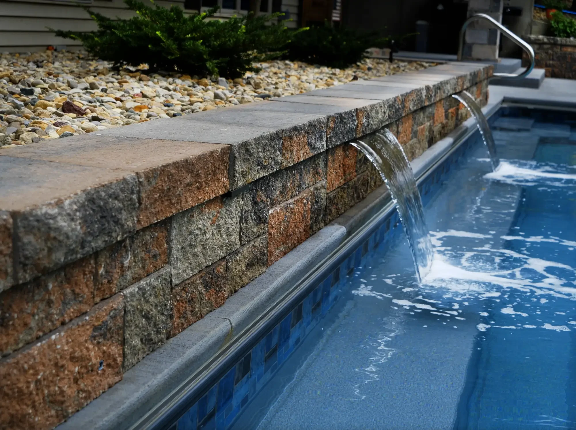 Stone retaining wall with built-in water feature cascading into pool at The Amphitheater by Green View in Illinois
