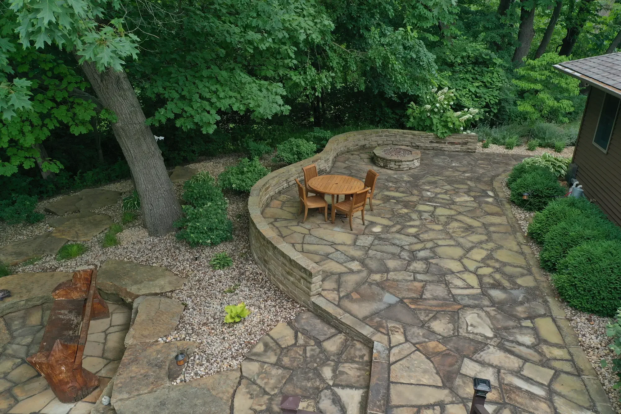 Aerial view of flagstone patio with outdoor dining set and stone fire pit surrounded by natural landscaping by Green View in Central Illinois