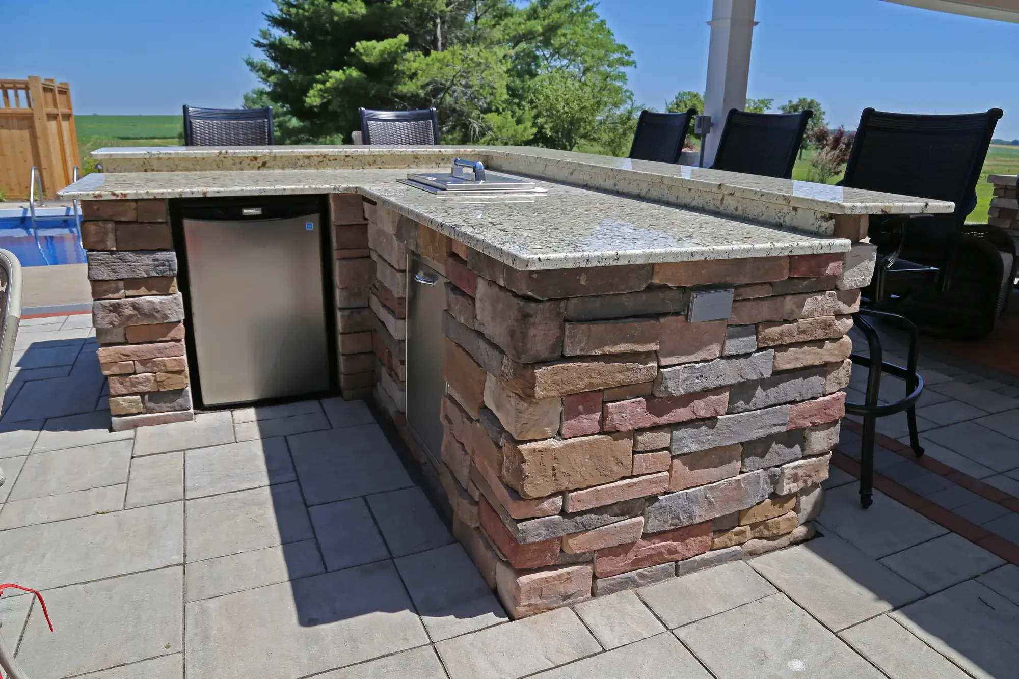 Stone outdoor bar with granite countertop and built-in stainless refrigerator at The Prairie Pavilion by Green View in Illinois