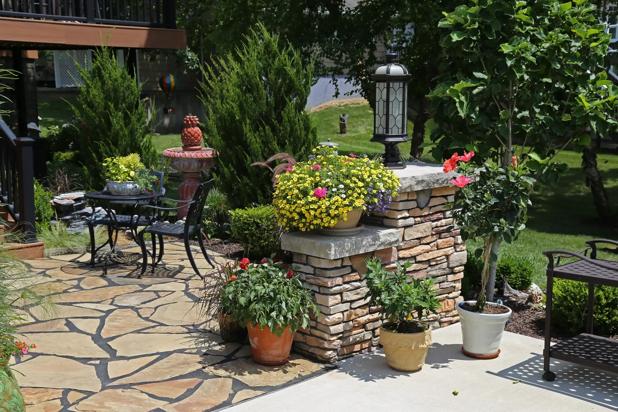 Flagstone patio with stacked stone column, colorful container plantings, and ornamental fountain at The Lakeside Garden by Green View in Illinois