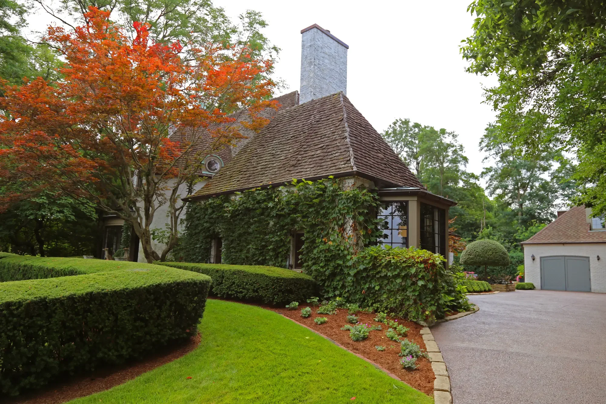 Estate exterior with ivy-covered facade, Japanese maple, curved clipped hedges, and mulched planting beds at The Tudor Knot Garden by Green View in Illinois