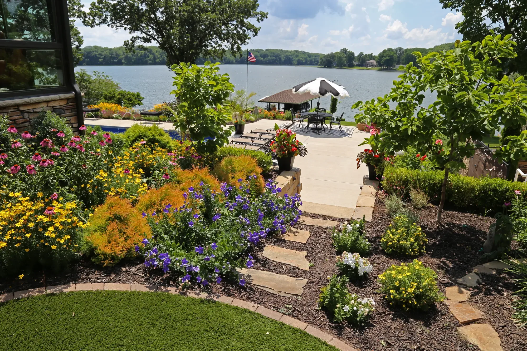 Perennial garden path with flagstone steps descending to pool patio and boat dock with open lake view at The Lakeside Garden by Green View in Illinois