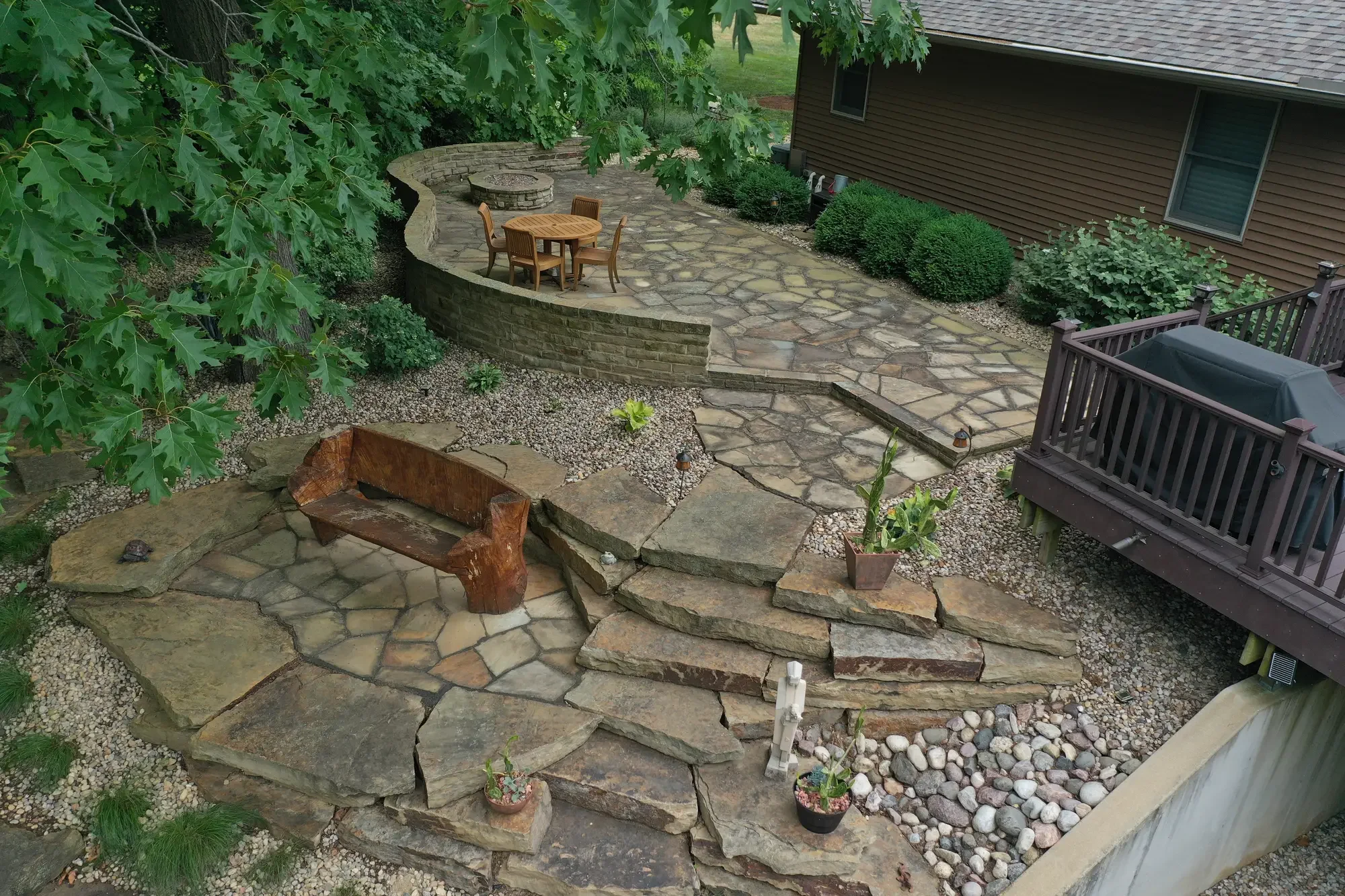 Aerial view of multi-level flagstone patio with raised stone seating wall and wood bench by Green View in Central Illinois