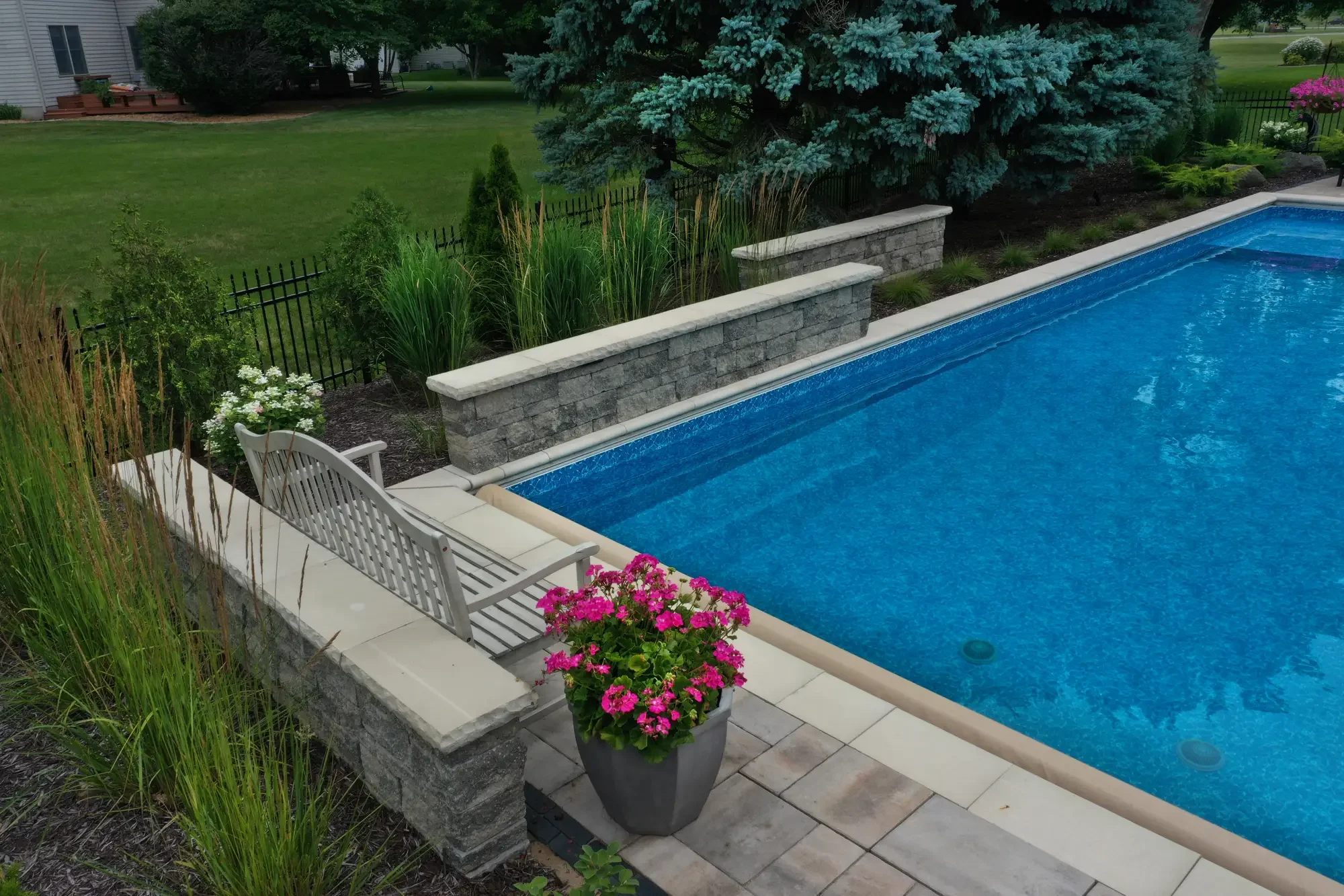 Stone pool wall with natural cap, ornamental grasses, and perennial planting by Green View in Illinois