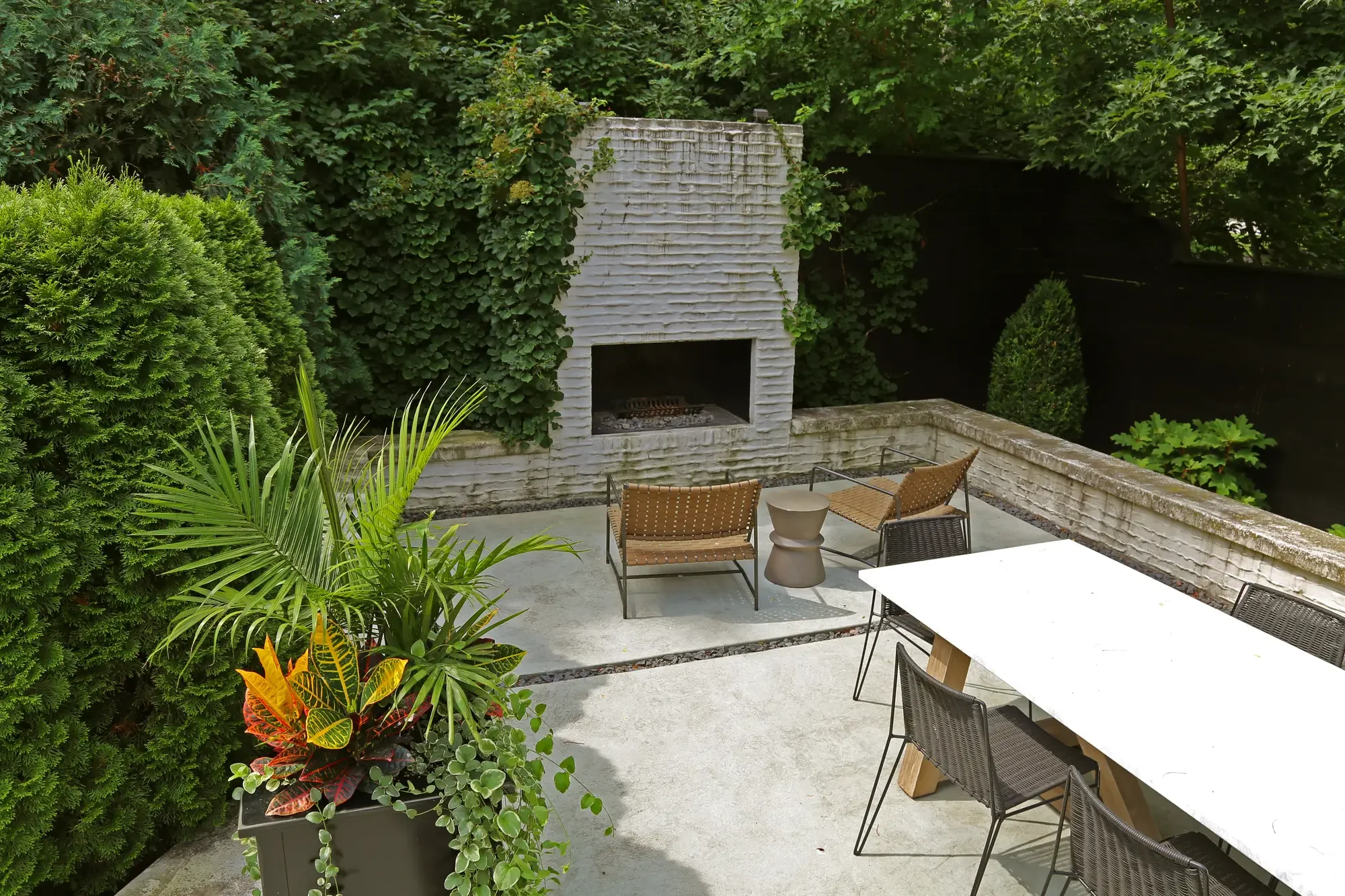 Sunken outdoor fireplace courtyard with lounge seating, dining table, and tropical container plantings at The Tudor Knot Garden by Green View in Illinois