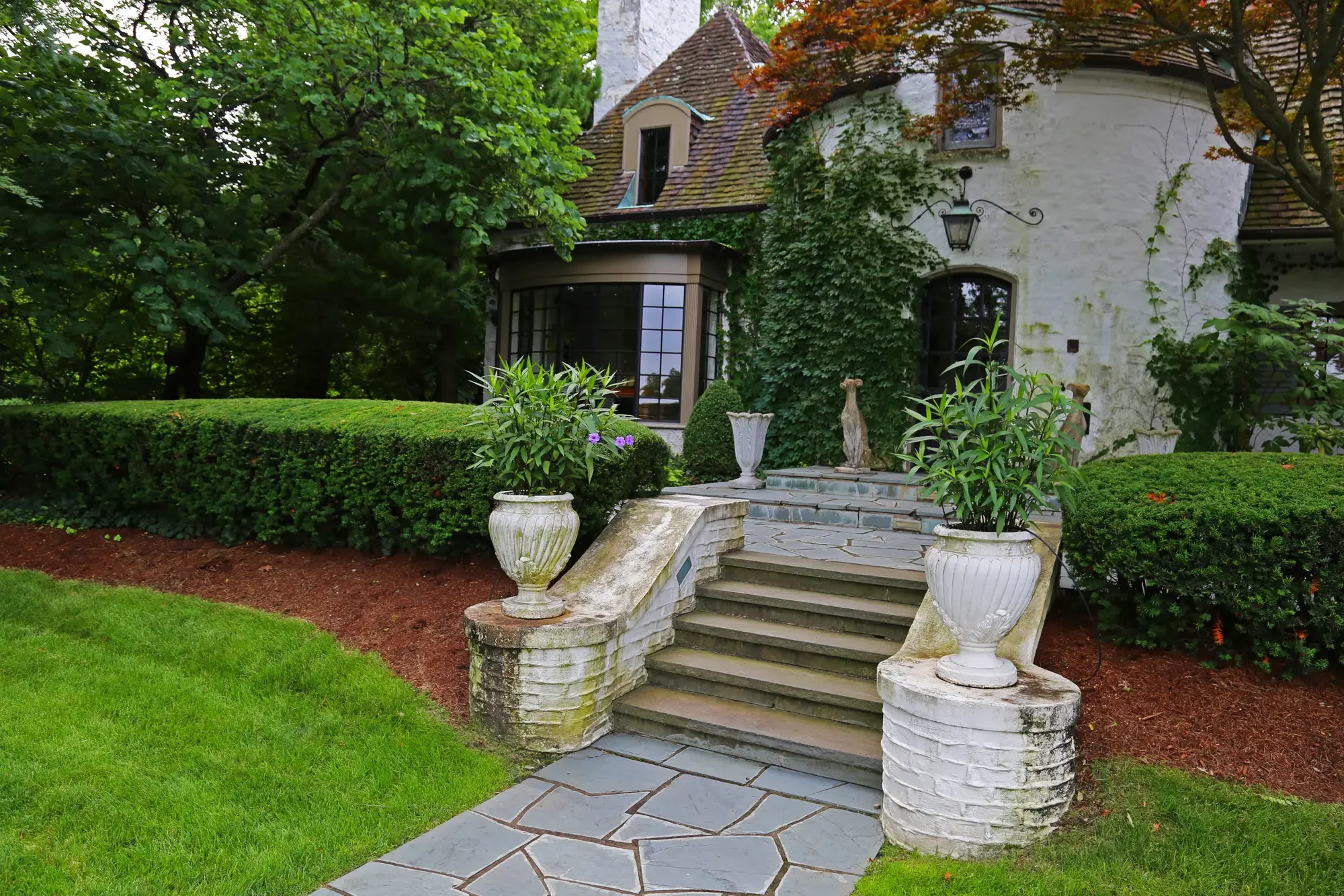 Flagstone entry walk with stone urn planters flanking steps to ivy-covered estate entrance at The Tudor Knot Garden by Green View in Illinois