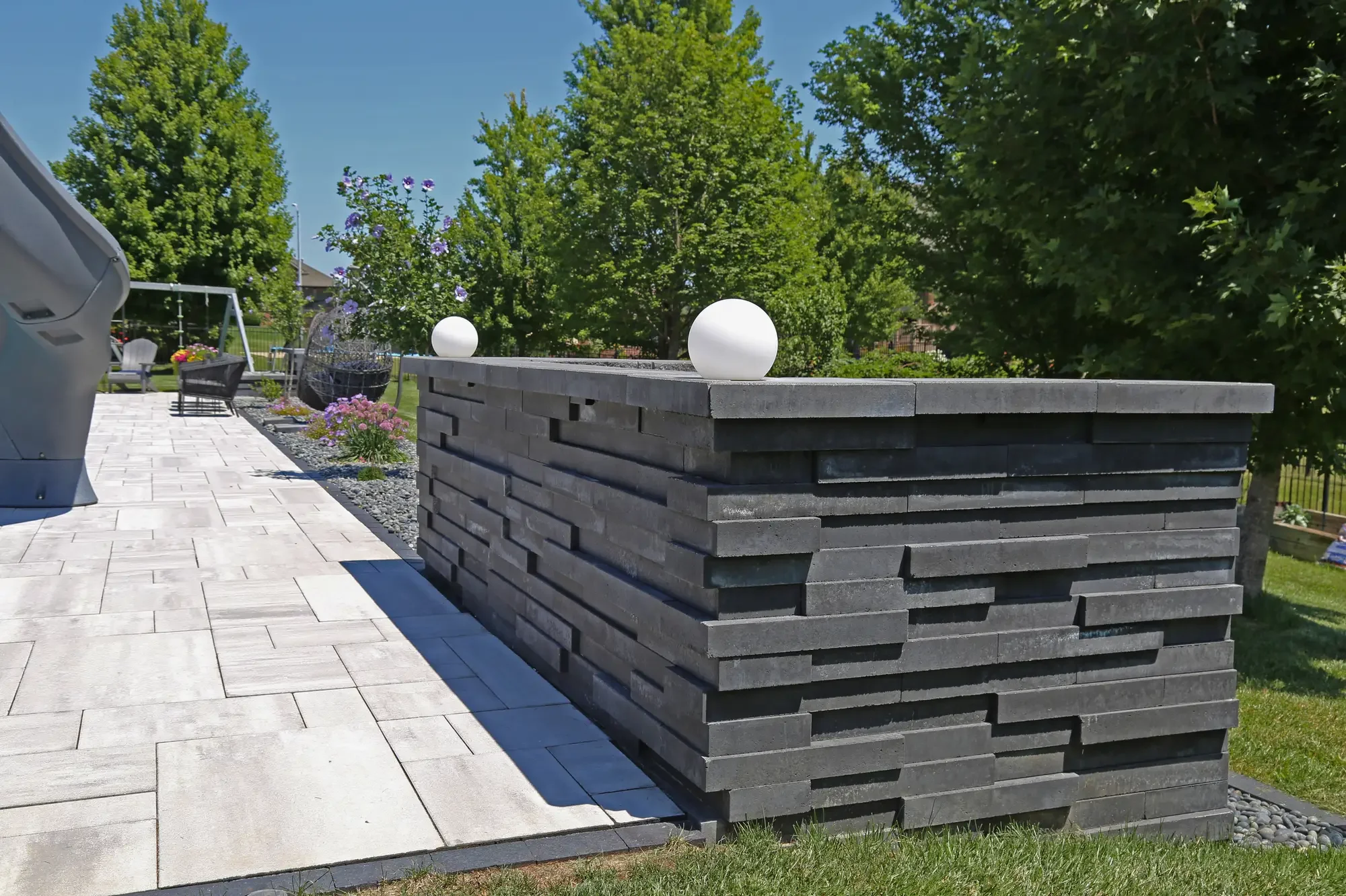 Dark stacked stone retaining wall with globe accent lights along large-format paver patio at Slate and Steel by Green View in Illinois