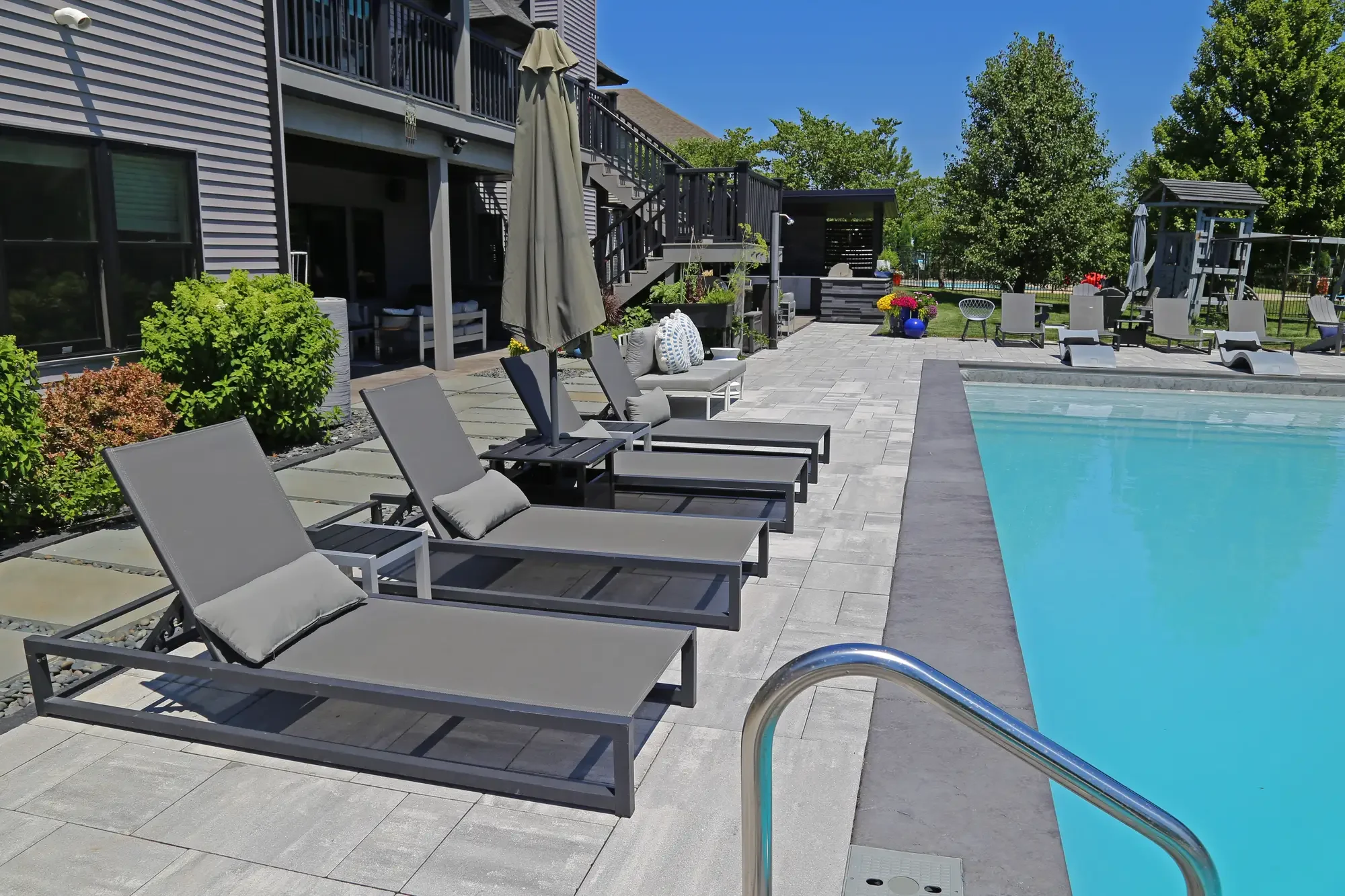 Row of modern chaise lounges along pool edge with paver patio and pergola in background at Slate and Steel by Green View in Illinois