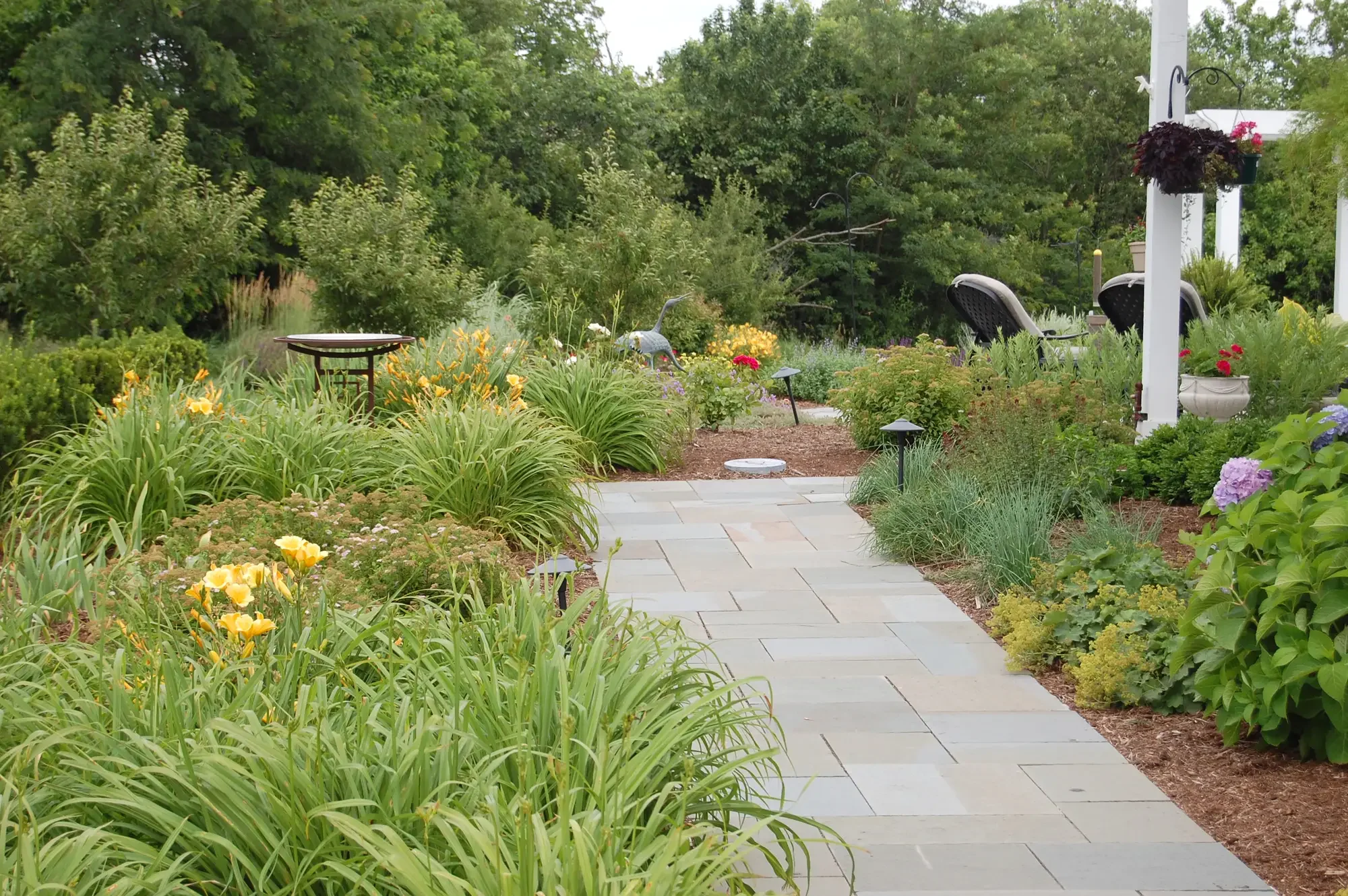 Bluestone garden path through daylily and perennial planting beds leading to white pergola at Harmony in Stone and Water by Green View in Illinois