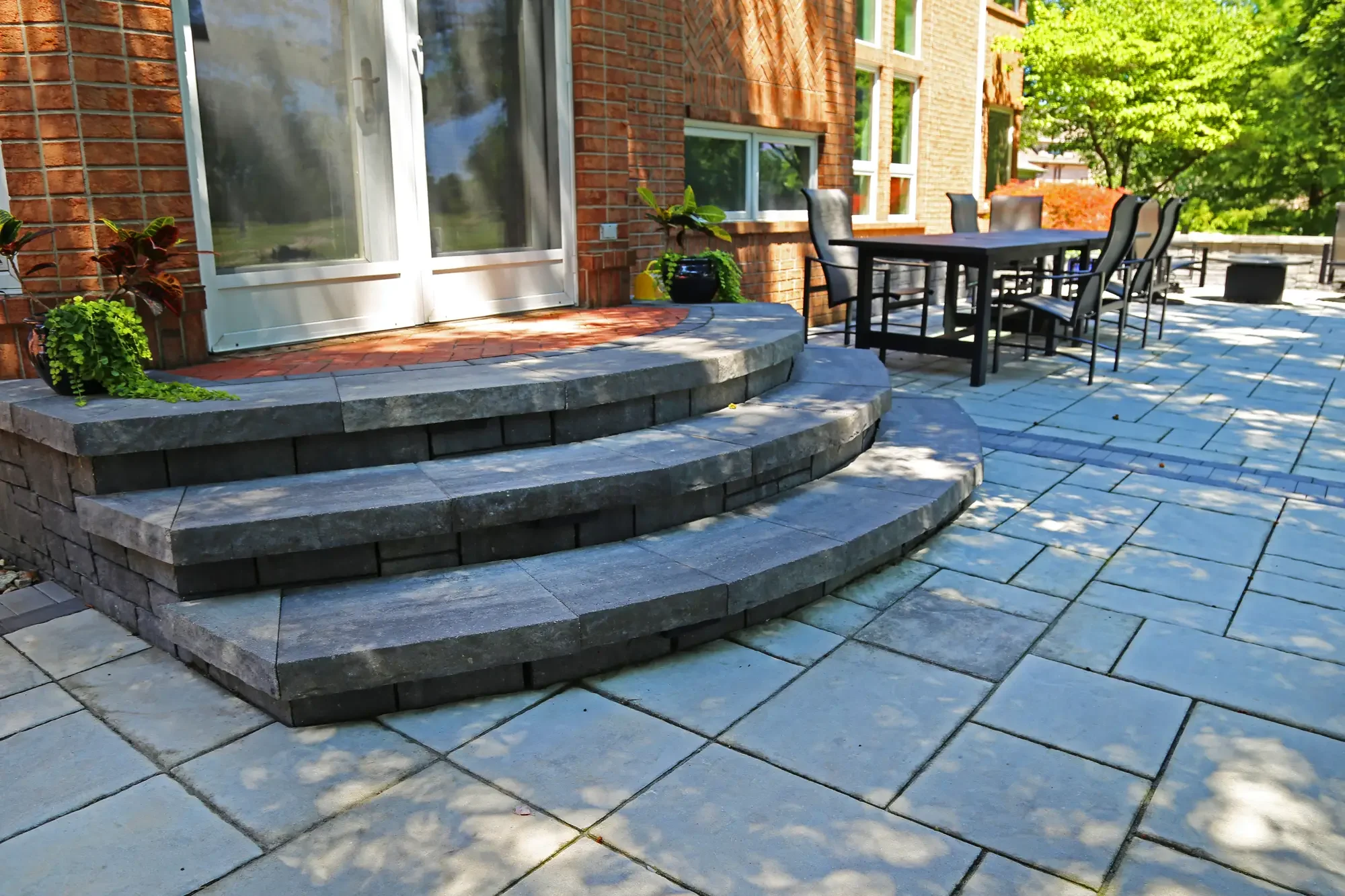 Curved paver steps descending from back door to large-format paver patio with dining area at The Wooded Pavilion by Green View in Illinois