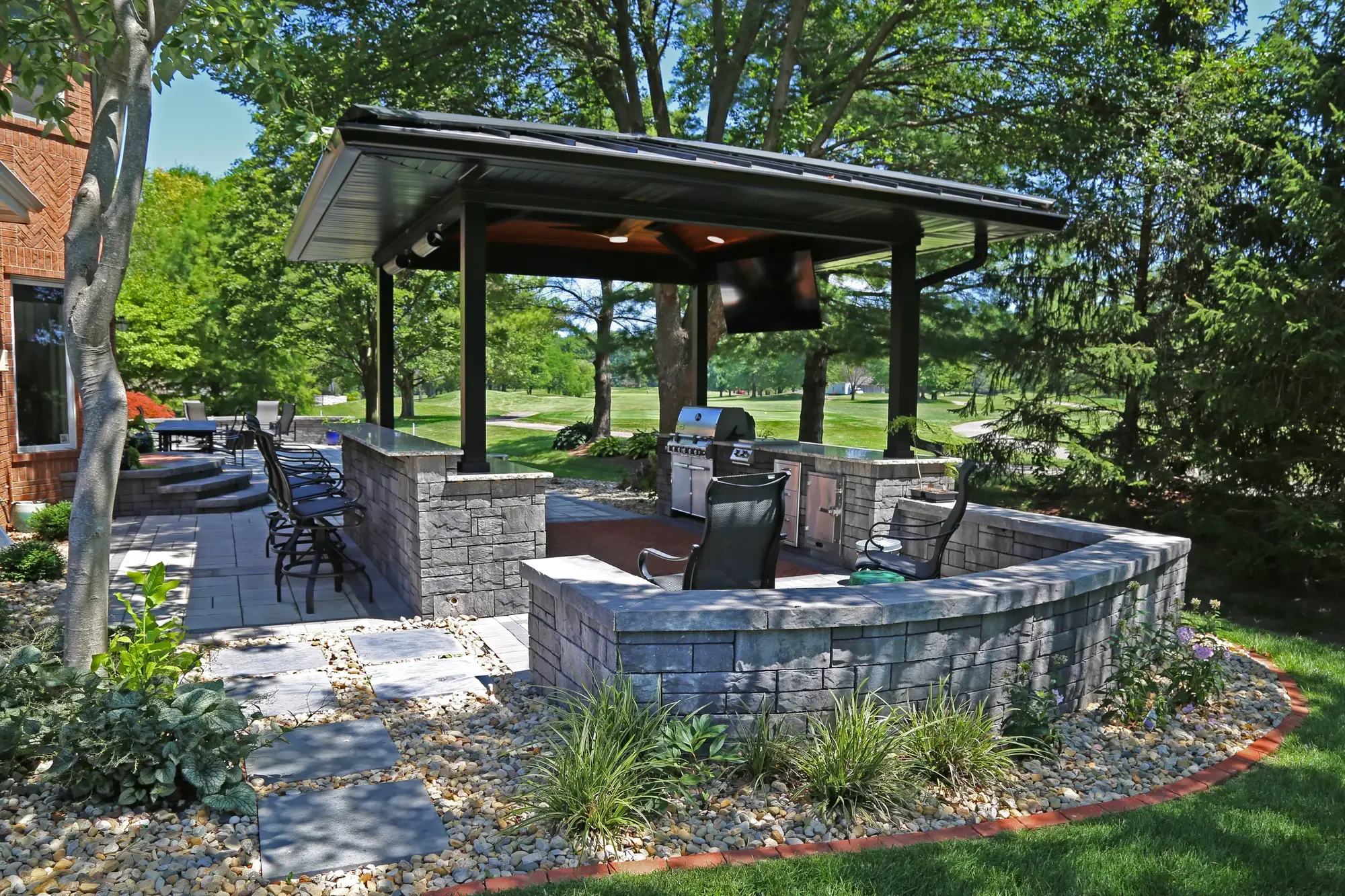 Dark pavilion with outdoor kitchen, curved stone seating wall, and open golf course view at The Wooded Pavilion by Green View in Illinois