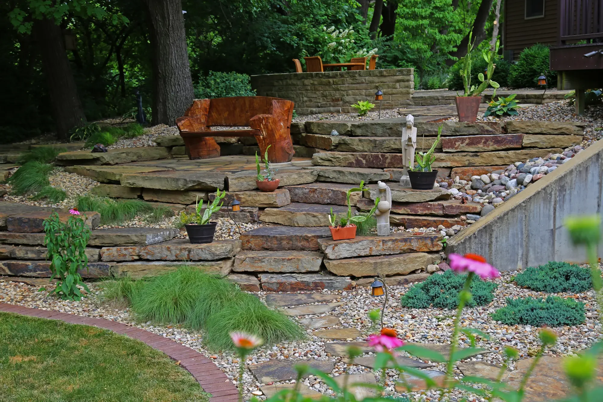 Layered stone steps with coneflowers, ornamental grasses, and potted plants leading to raised flagstone patio by Green View in Central Illinois
