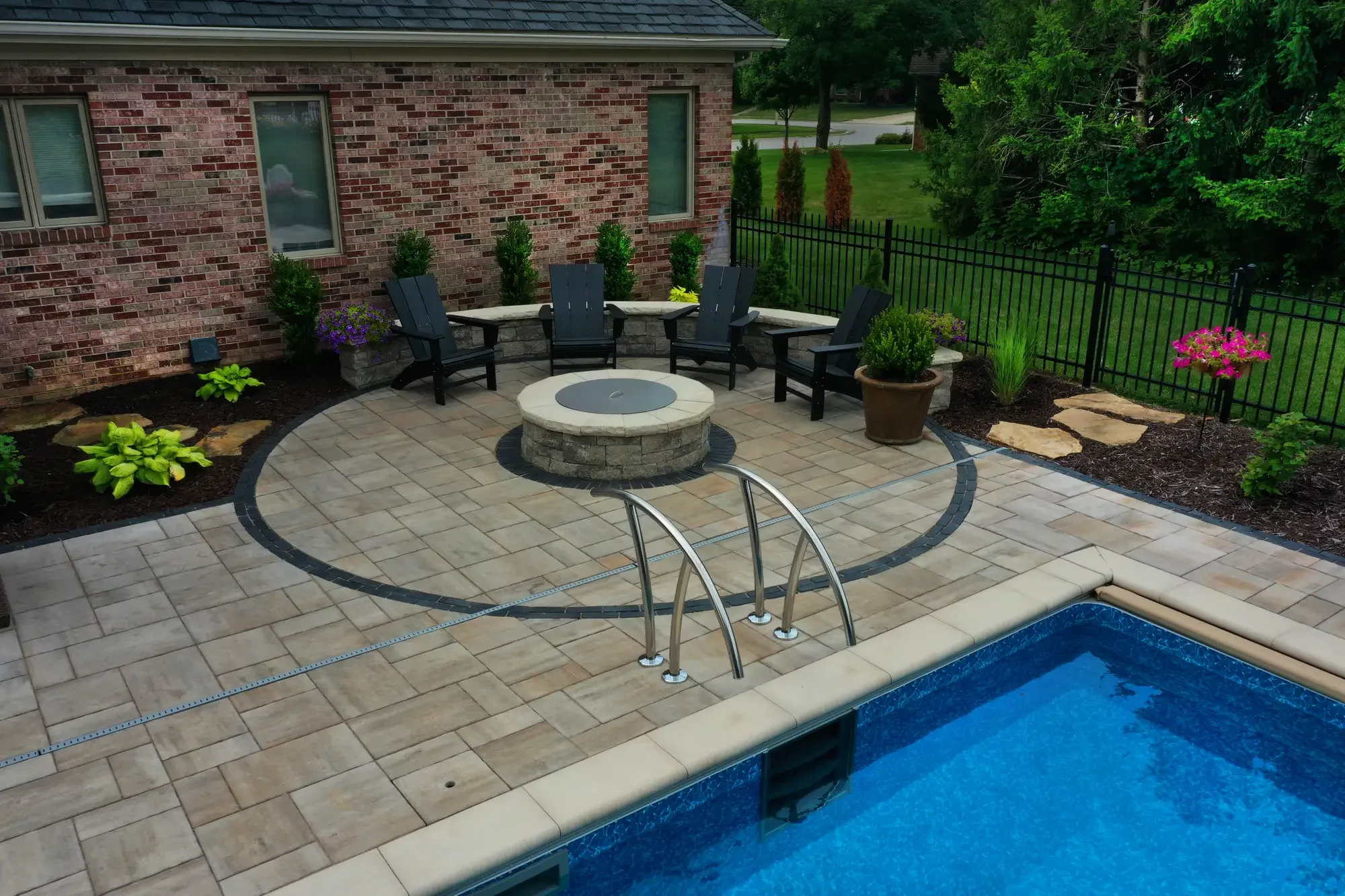Circular stone fire pit with paver patio and pool surround by Green View in Illinois